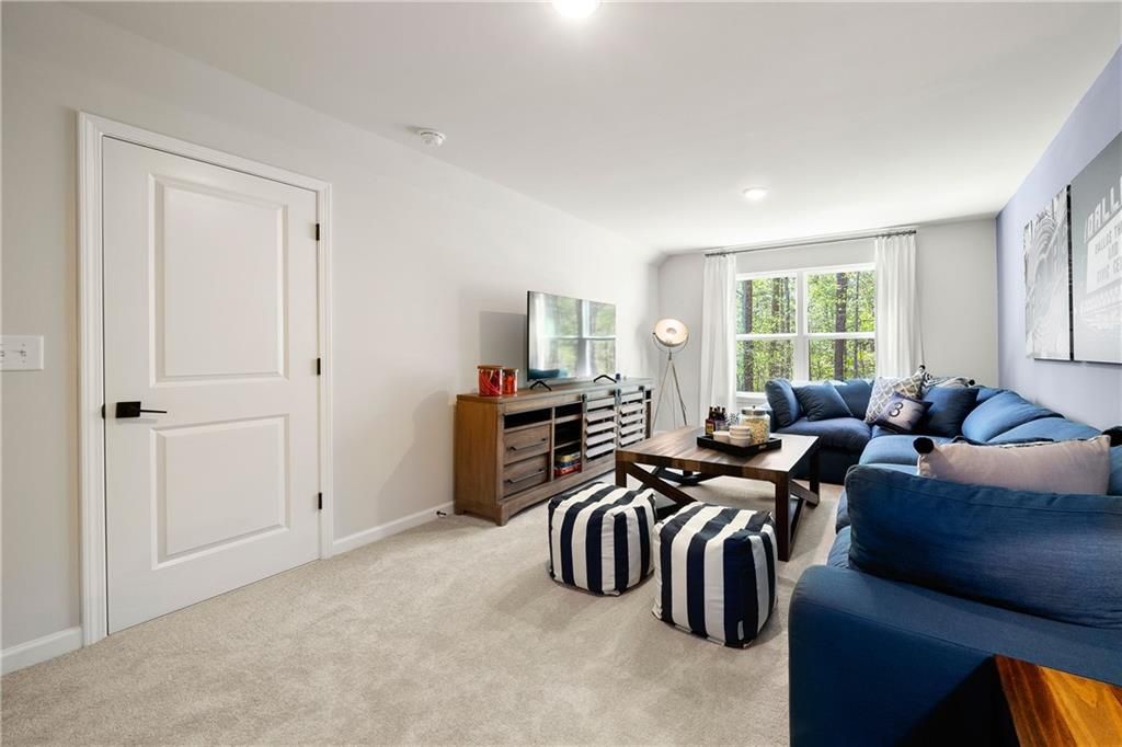 Bonus room with blue sectional sofa, TV console, striped poufs, and large windows in Davidson Homes The Willow B, Riverwood, Dallas, Georgia