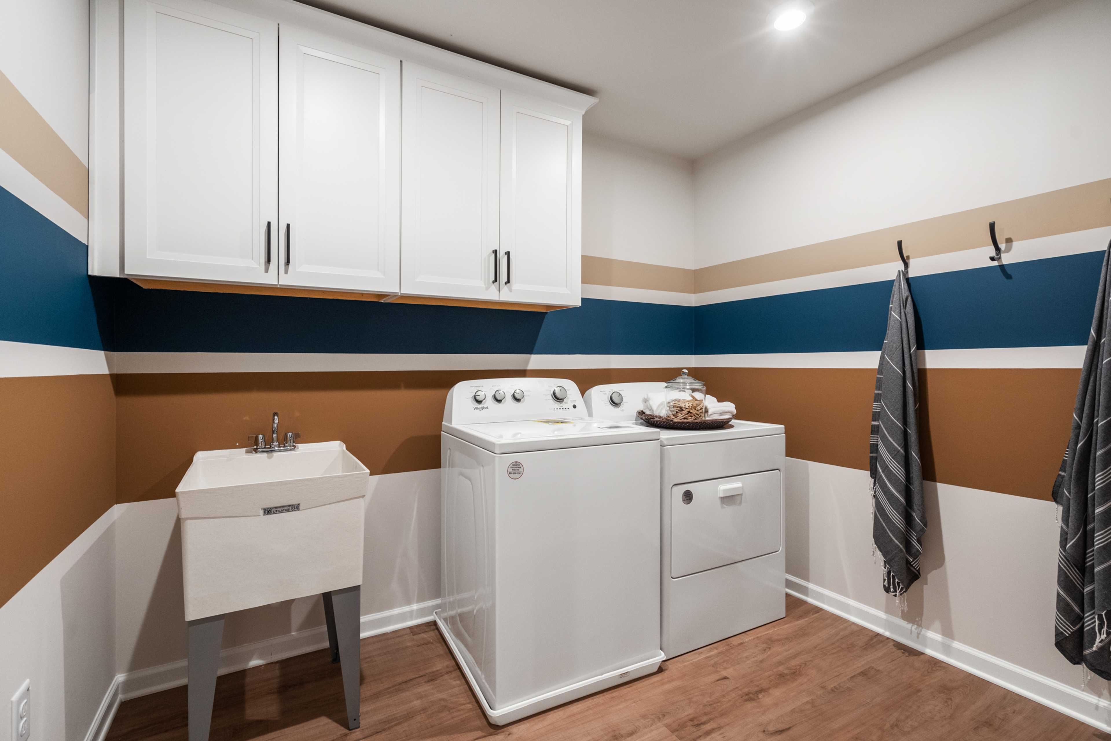 Spacious laundry room at The Village at Shallowford in Kennesaw GA with white washer dryer sink cabinets and striped walls