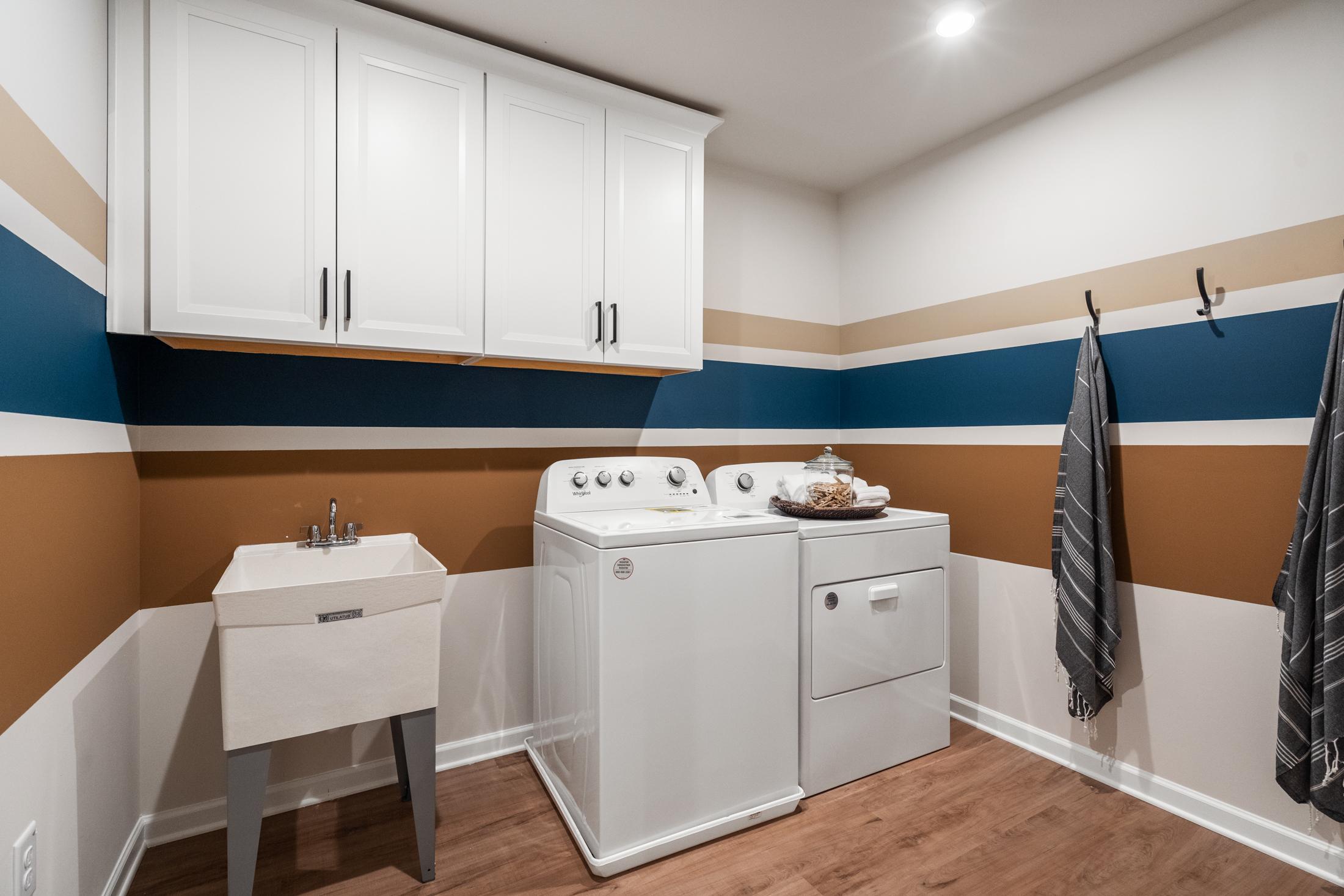 Spacious laundry room in The Marion A by Davidson Homes with white washer dryer, utility sink, striped navy beige walls, hardwood floors