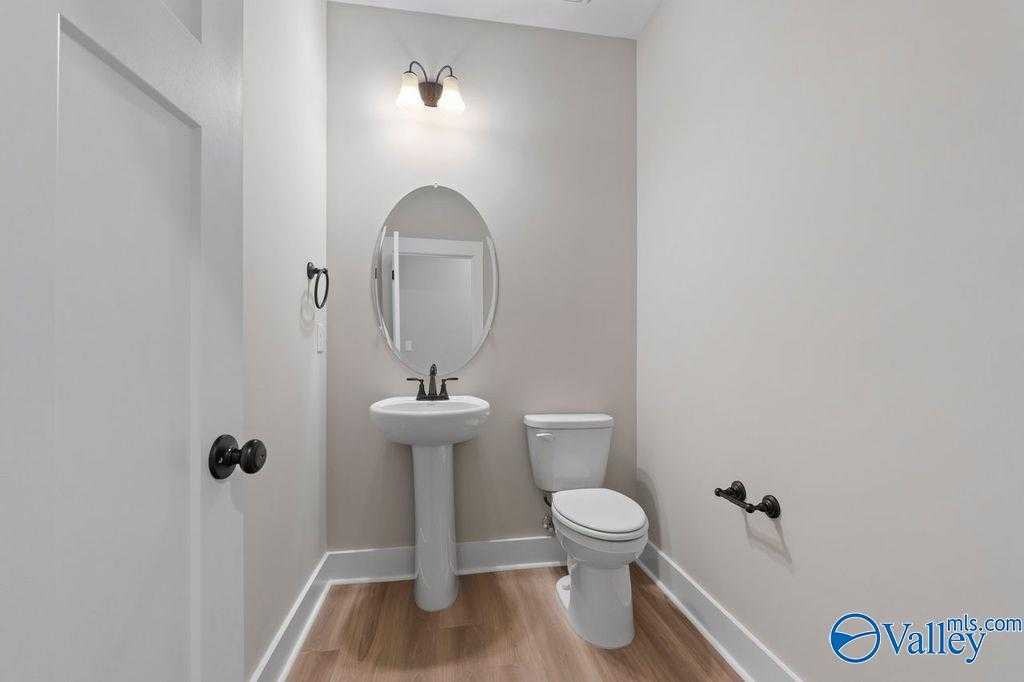 Elegant powder room featuring pedestal sink, round mirror, and light gray walls in Evermore Homes The Oxford, Owens Cross Roads, Alabama