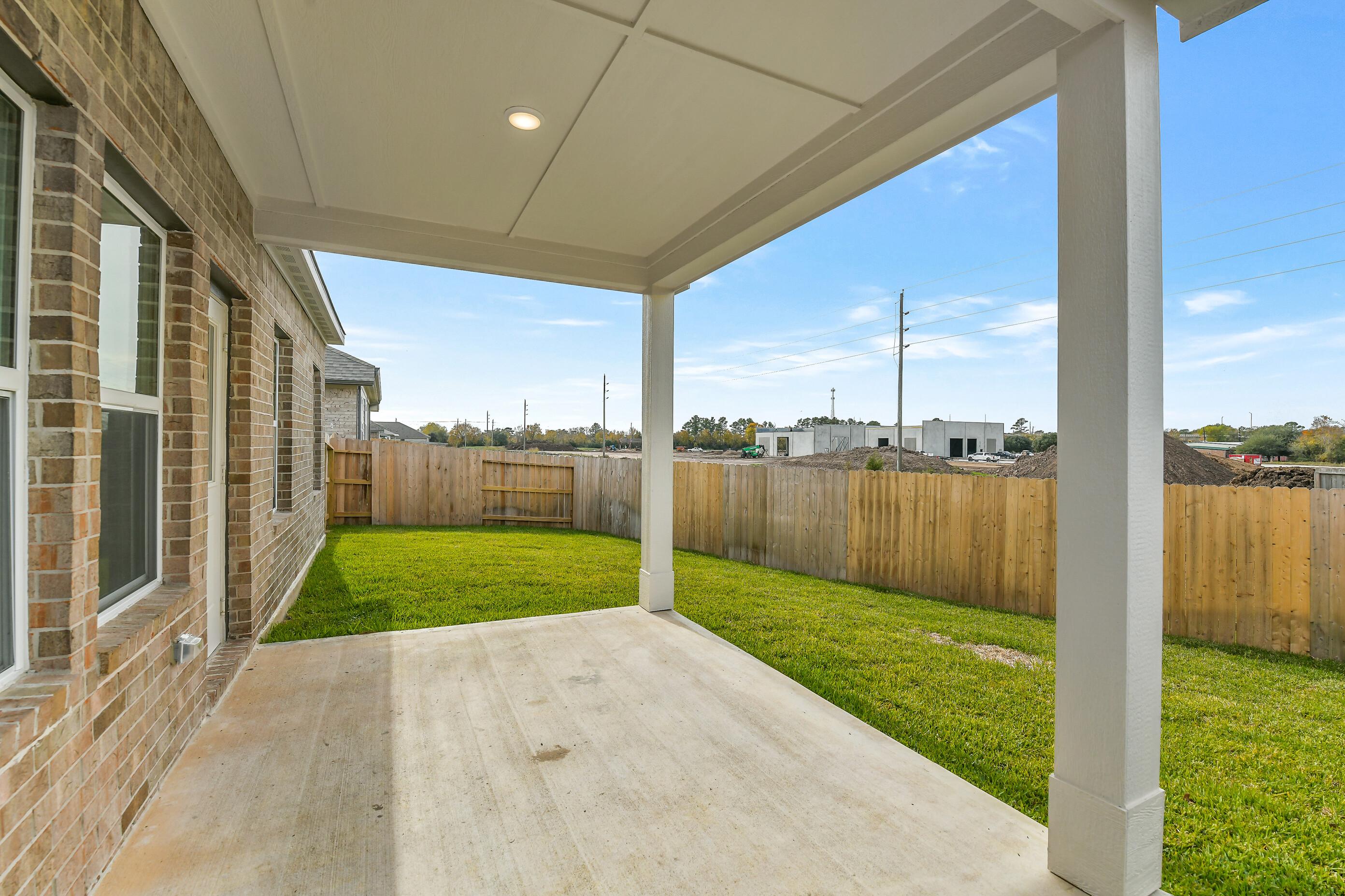 Covered patio with white columns and concrete slab overlooking lush green backyard in 4-bedroom Davidson Homes The Colorado G, Windmill Estates, Magnolia, Texas
