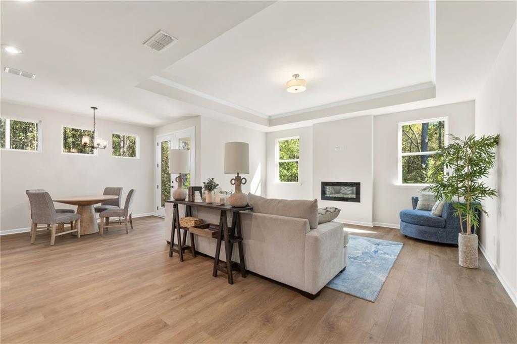 Open-concept living room with gas fireplace, beige sofa, round dining table, and hardwood floors in Davidson Homes The Daphne B, Loganville, GA
