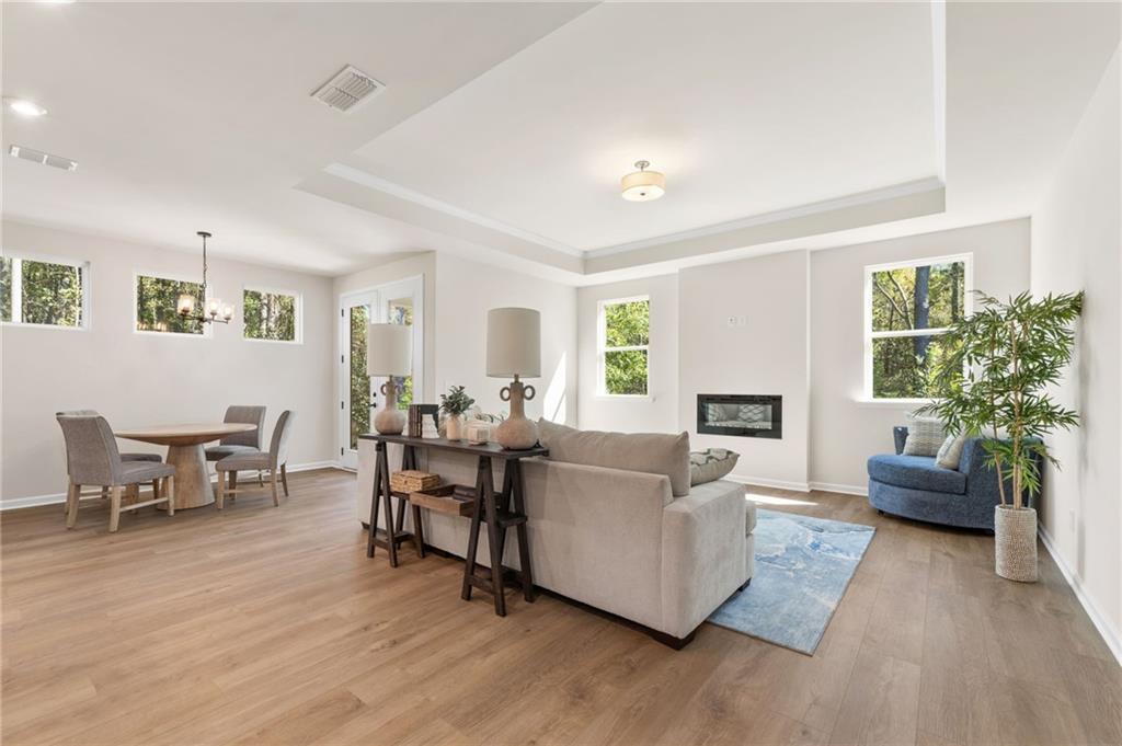 Open-concept living room with gas fireplace, L-shaped sofa, dining table, and large windows in Davidson Homes The Daphne B, Loganville, GA