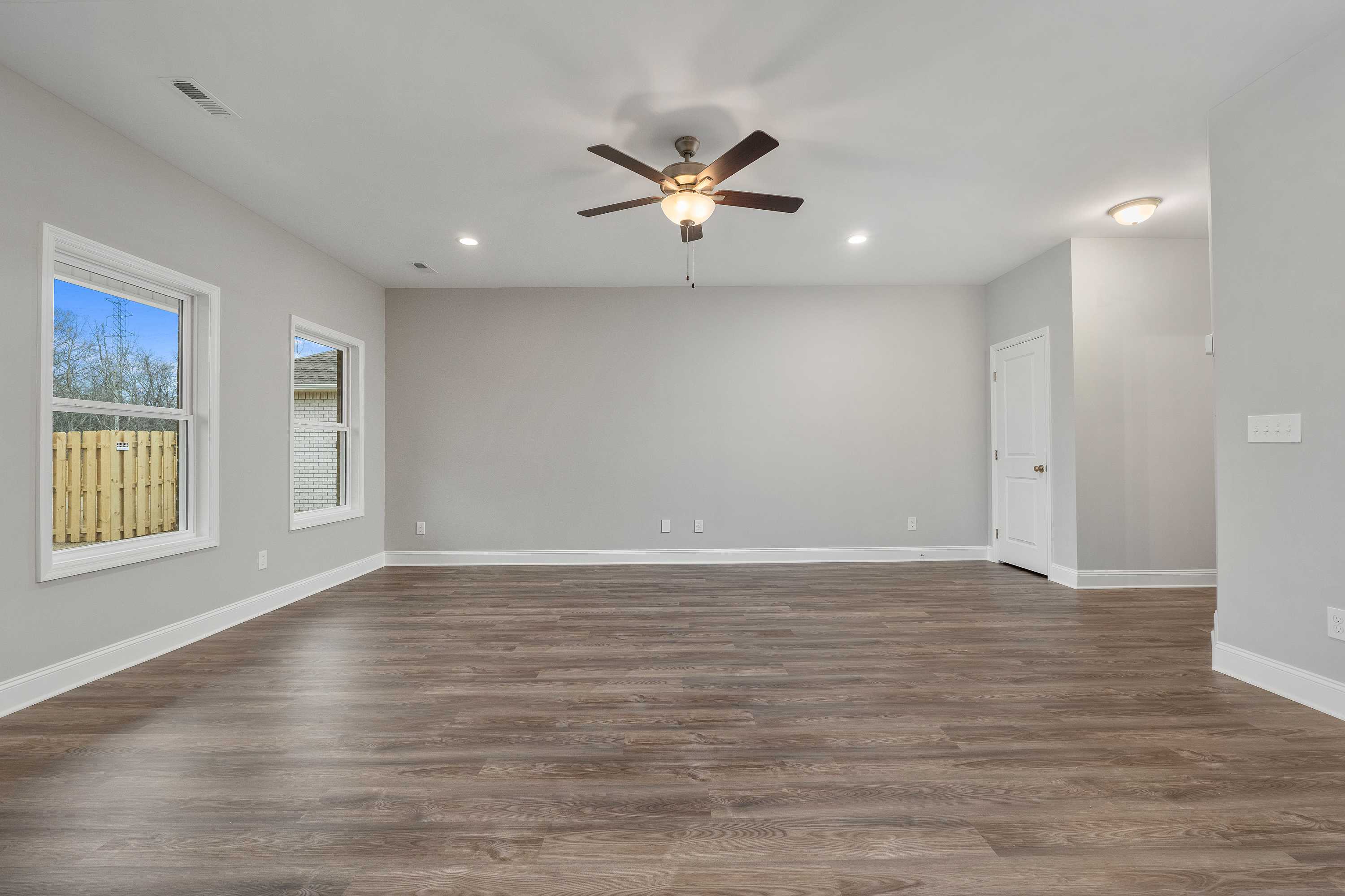 Spacious empty living room in The Aiken with gray walls, hardwood floors, ceiling fan, and large windows