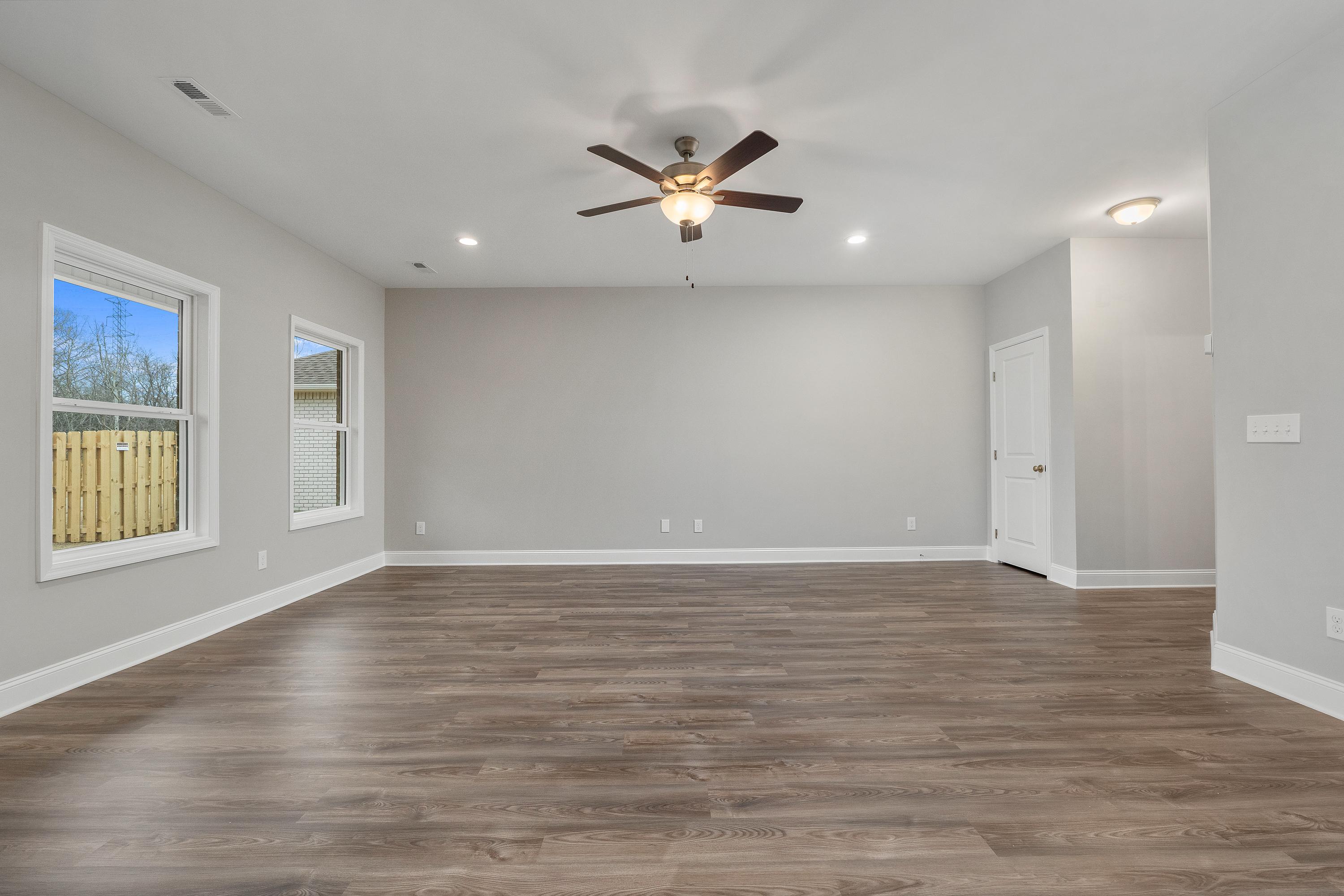 Spacious empty living room in The Aiken with gray walls, hardwood floors, ceiling fan, and large windows