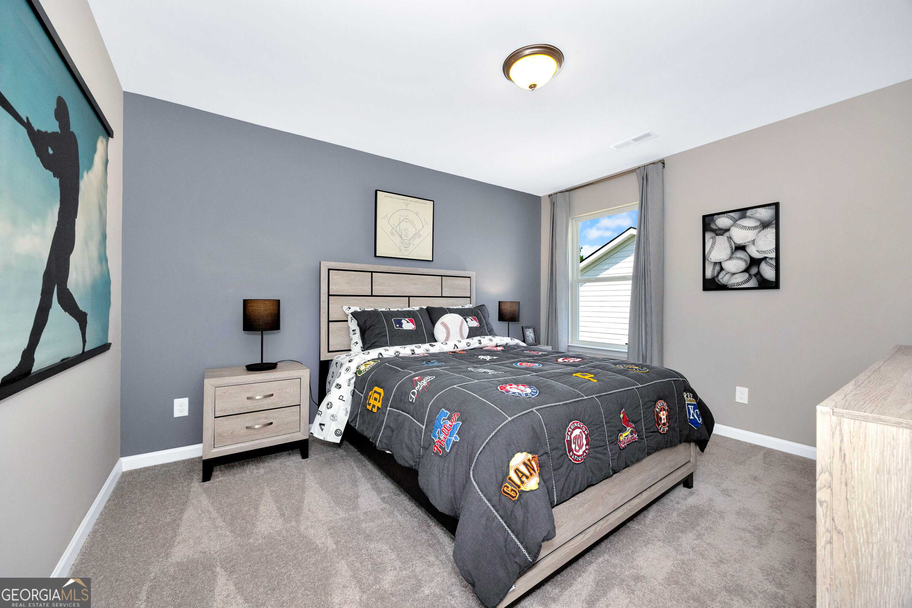 Sports-themed bedroom with baseball artwork, gray bedding on queen bed, nightstands in Evermore Homes The Stella, Perry, Georgia