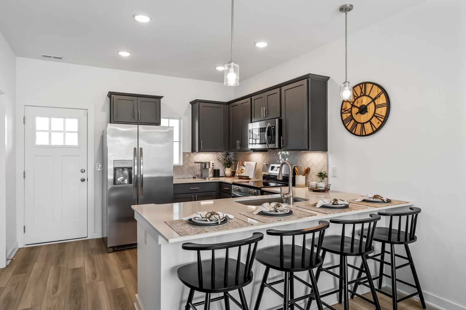 Modern gray shaker kitchen with stainless appliances, quartz island, and bar stools in Davidson Homes Cumberland B, Gallatin, TN