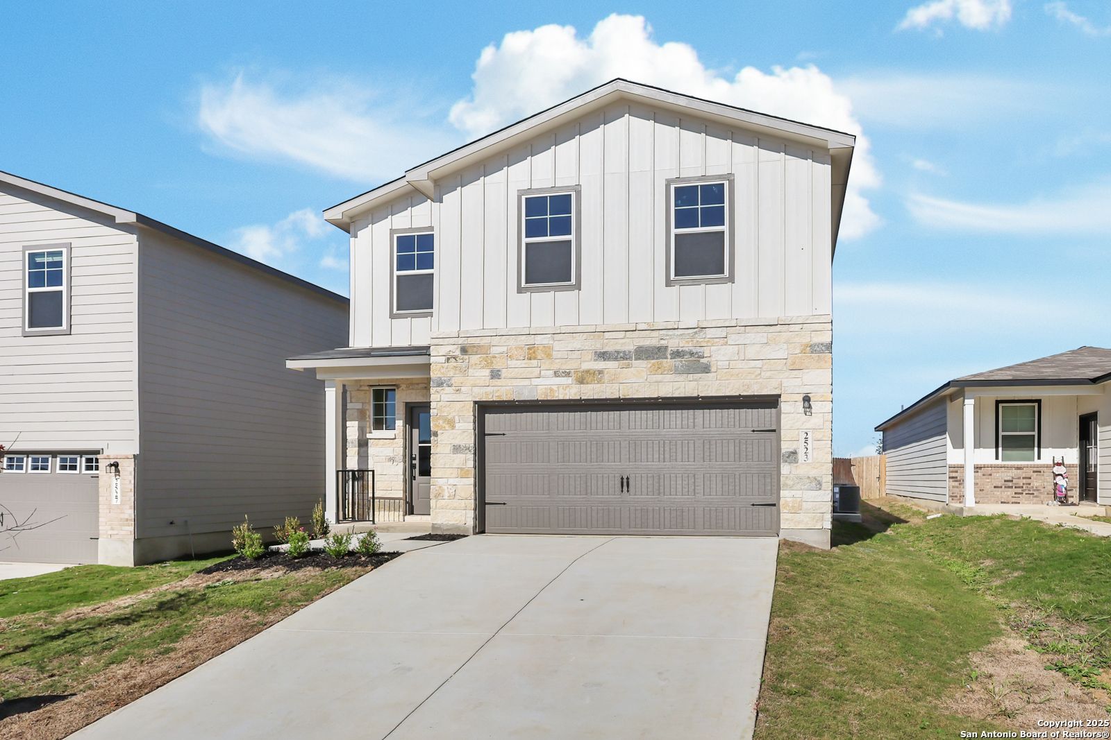 Modern two-story home with white board-and-batten siding, stone accents, two-car garage, and front porch in Applewhite Meadows, San Antonio