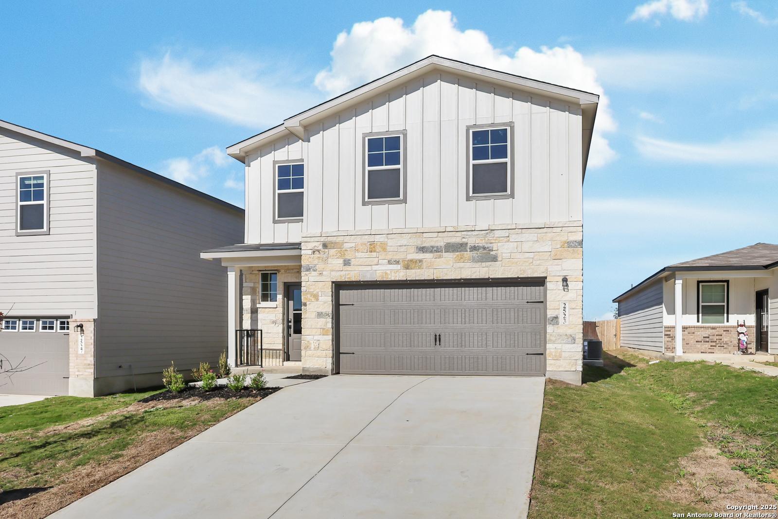 Modern two-story home with white board-and-batten siding, stone accents, two-car garage, and front porch in Applewhite Meadows, San Antonio