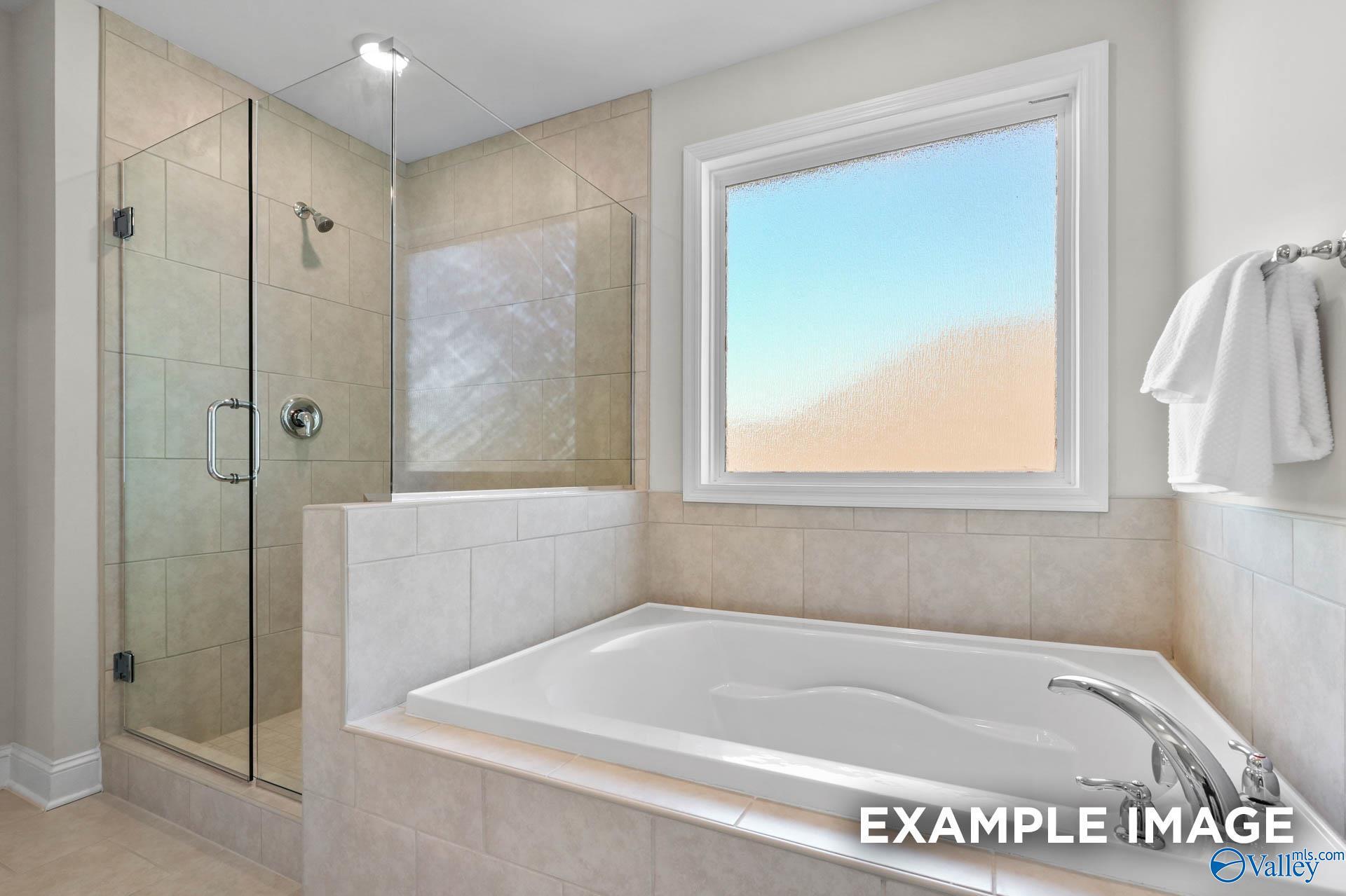 Modern primary bathroom with a tiled walk-in glass shower and soaking tub in The Madison A home, The Meadows, Athens, AL.