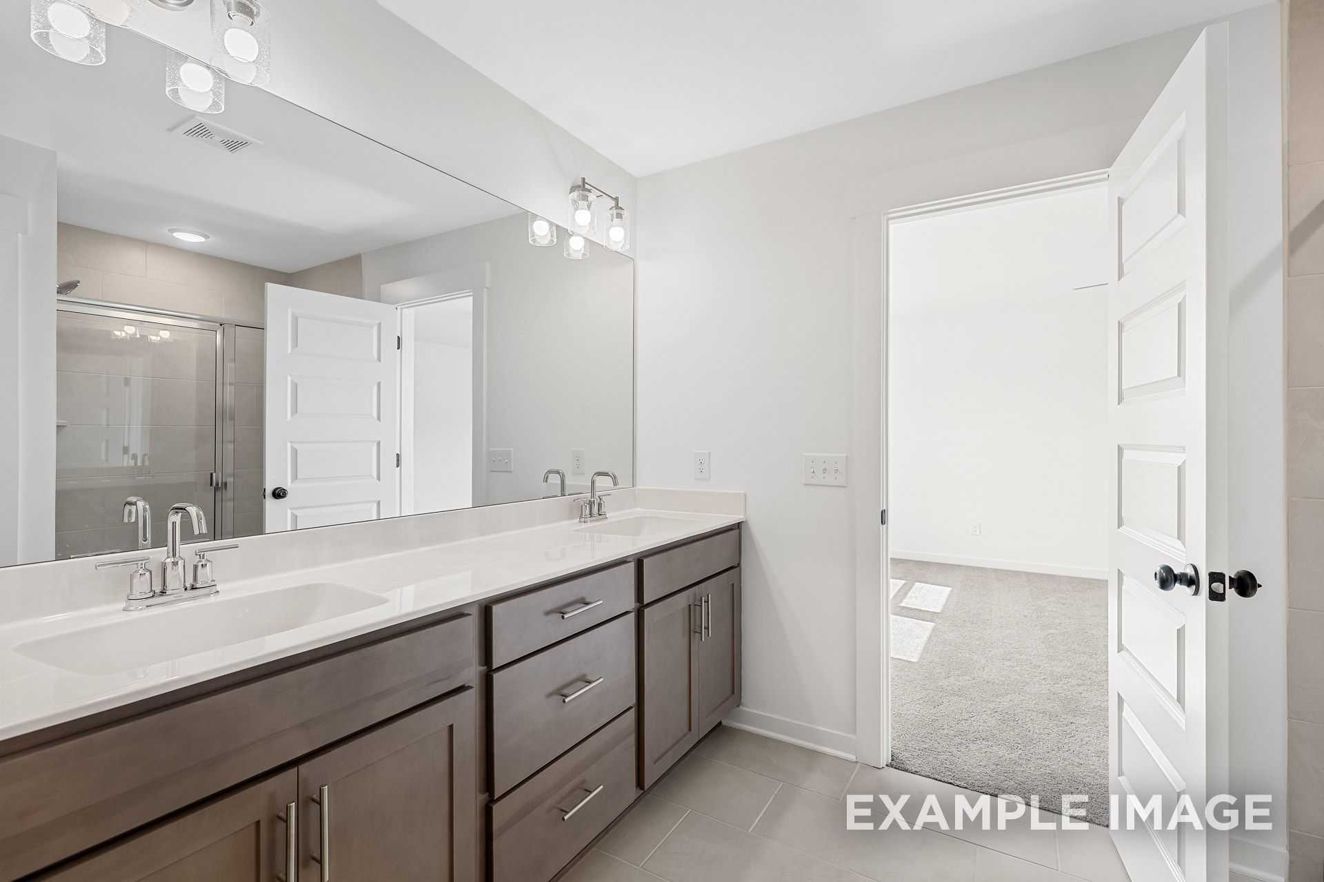 Spacious master bathroom in The Logan B with double vanity, large mirror, and glass shower door