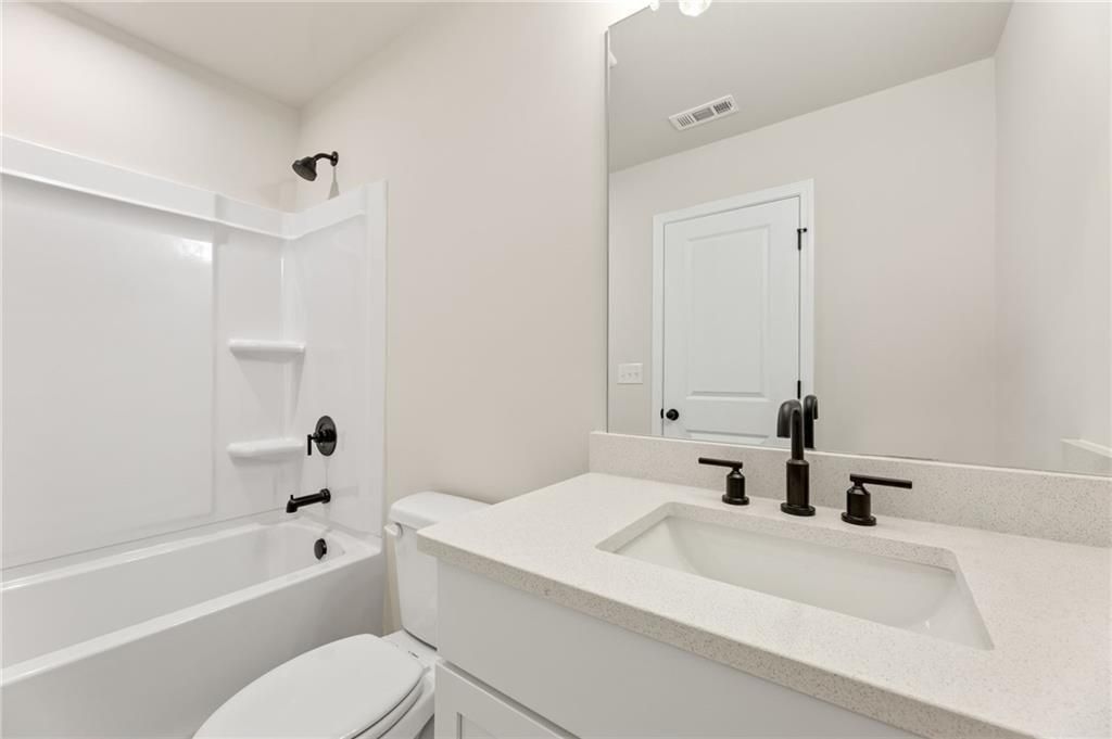 Modern bathroom with white tub, glass shower, quartz vanity and toilet in Davidson Homes Hickory E, Buford, Georgia