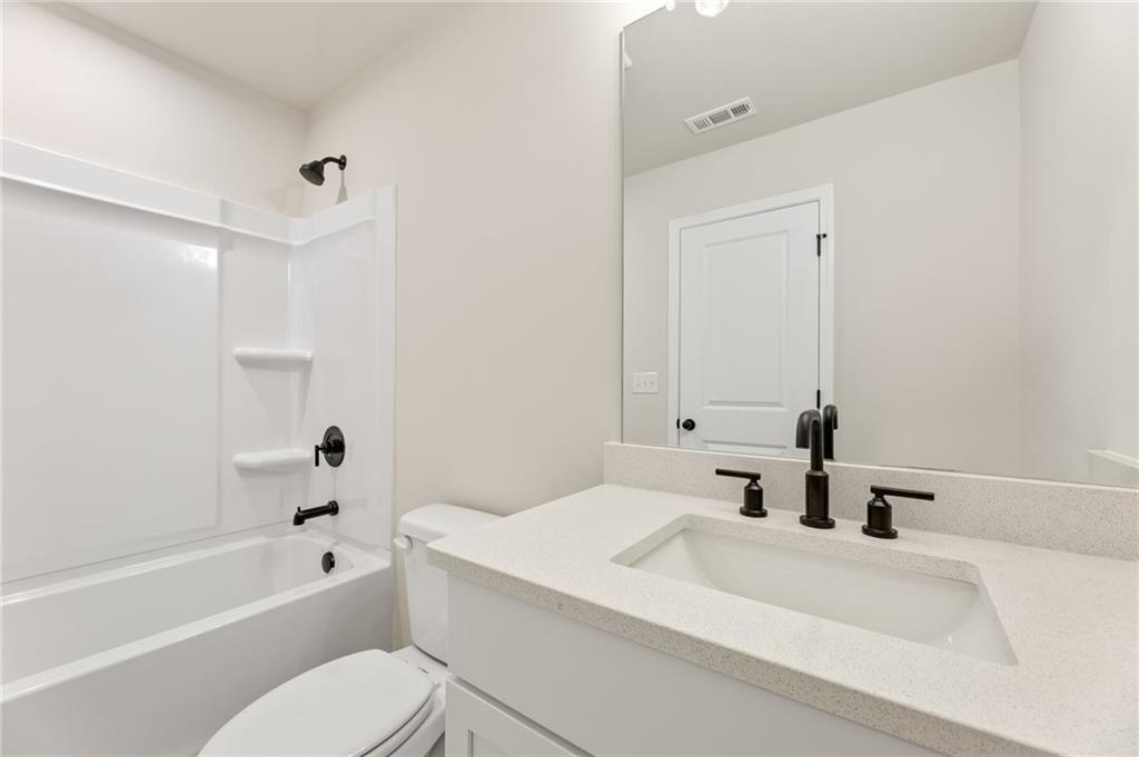 Modern bathroom with white tub, glass shower, quartz vanity and toilet in Davidson Homes Hickory E, Buford, Georgia