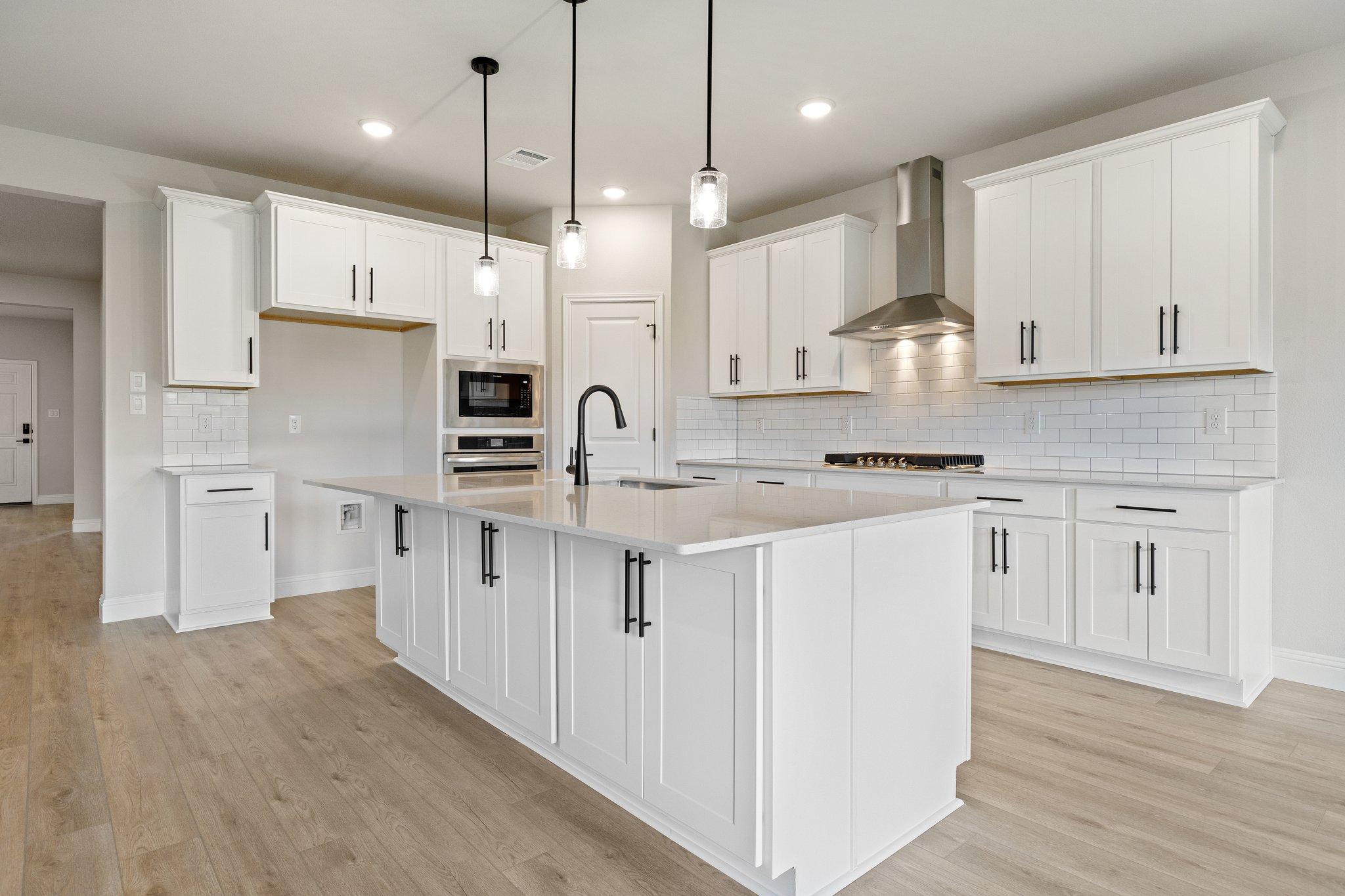 Spacious white kitchen in The Harrison with large island, subway tile backsplash, pendant lights, and hardwood floors