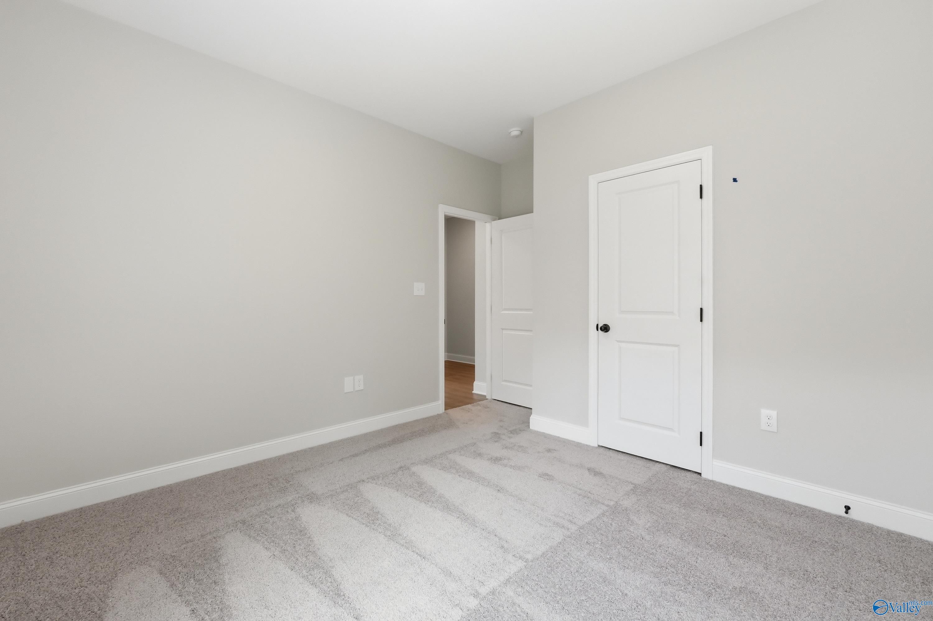 Empty secondary bedroom featuring light gray walls, plush gray carpet, and open door to adjacent room in Davidson Homes The Franklin, Huntsville AL