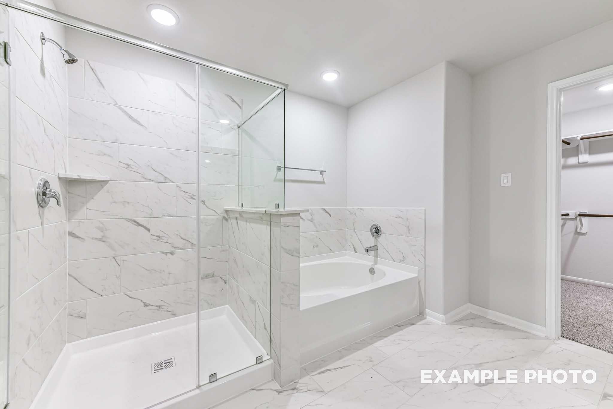 Modern bathroom with marble-style tile shower, soaking tub, and walk-in closet in The Laguna C home in Sunterra, Katy.
