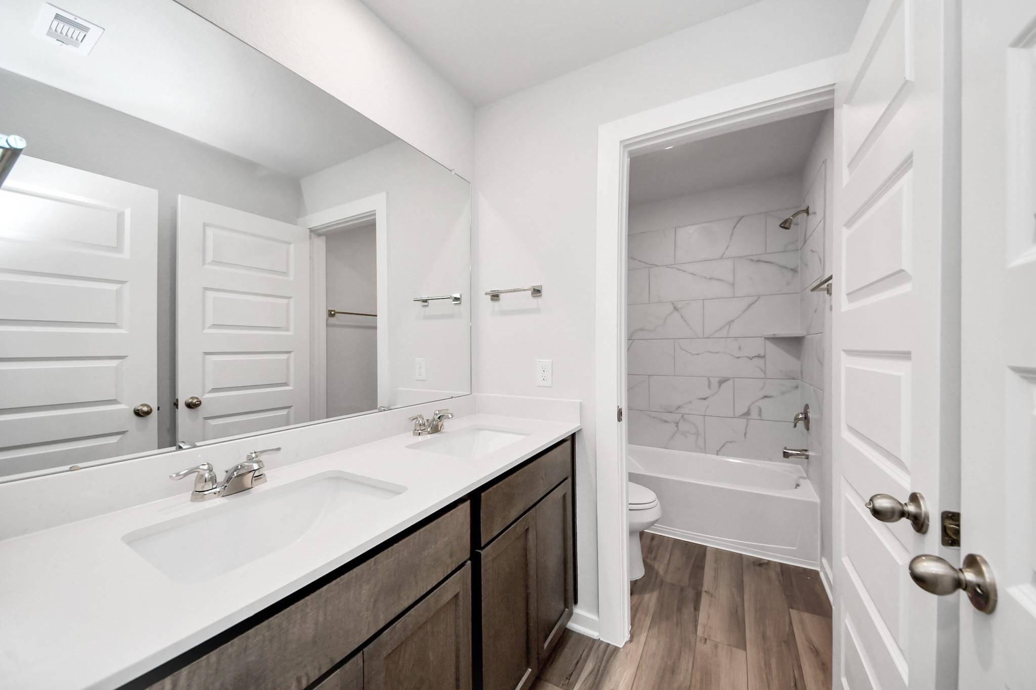 Modern bathroom with double vanity and marble-tiled tub shower in The Sabine E floor plan at Liberty Estates, Cleveland.