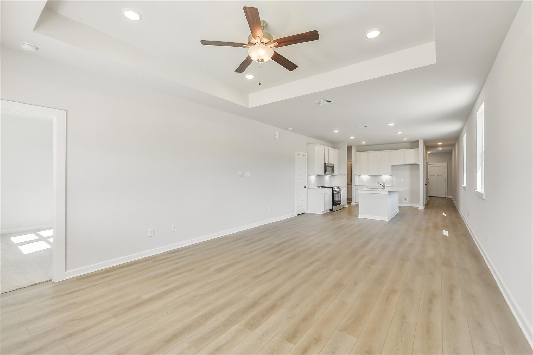 Open-concept living-kitchen with white cabinets, island, stainless appliances, laminate floors, ceiling fan in The Frio G, Conroe, Texas