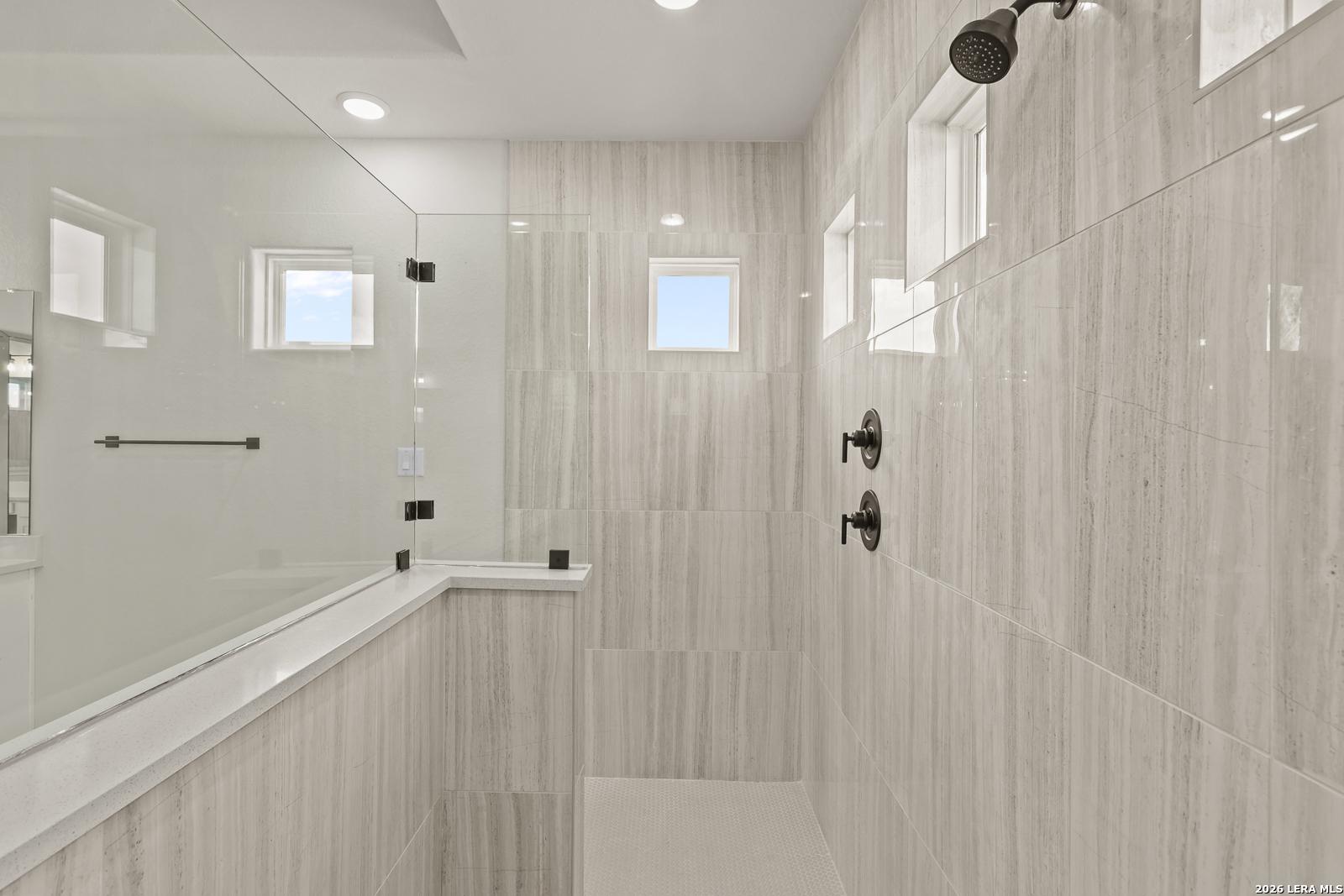 Modern walk-in shower with floor-to-ceiling tile in The Summerlin B floor plan by Davidson Homes in Castroville, Texas.