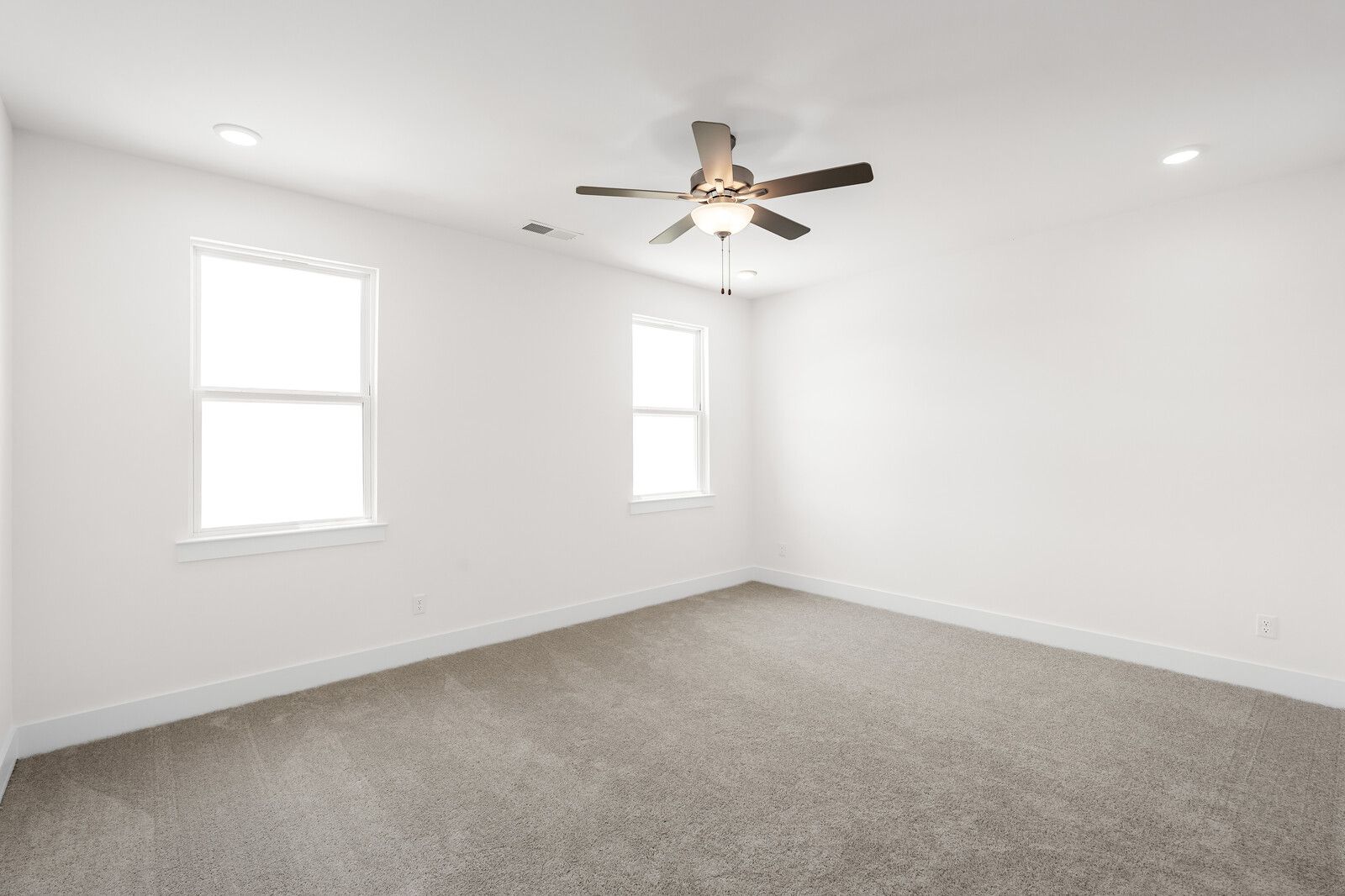 Spacious bedroom in The Cottonwood floor plan by Davidson Homes featuring neutral carpet, bright lighting, and ceiling fan.