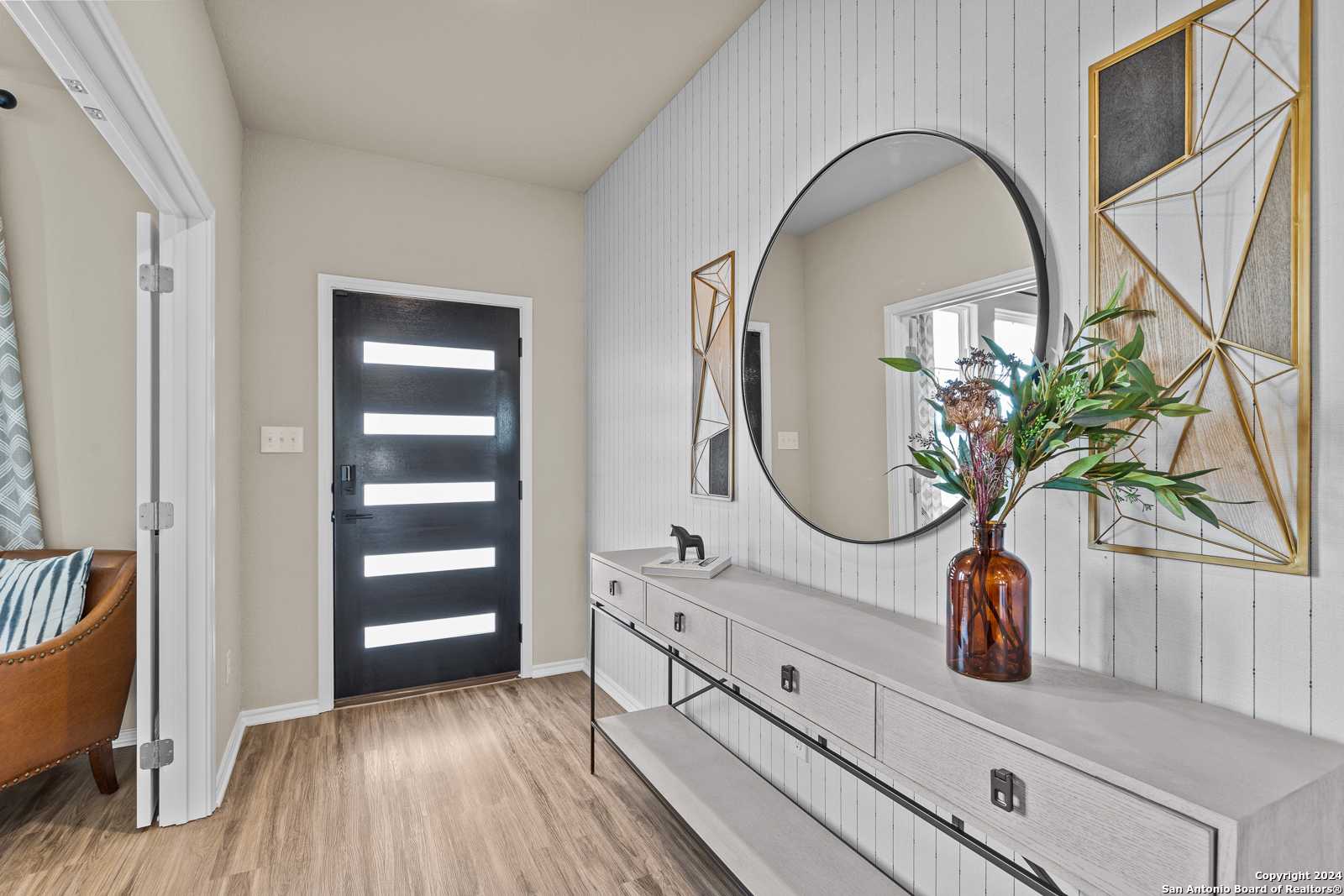 Elegant entryway with modern black door, shiplap wall, gold round mirror, and console table in Davidson Homes The Douglas F, Bricewood, San Antonio