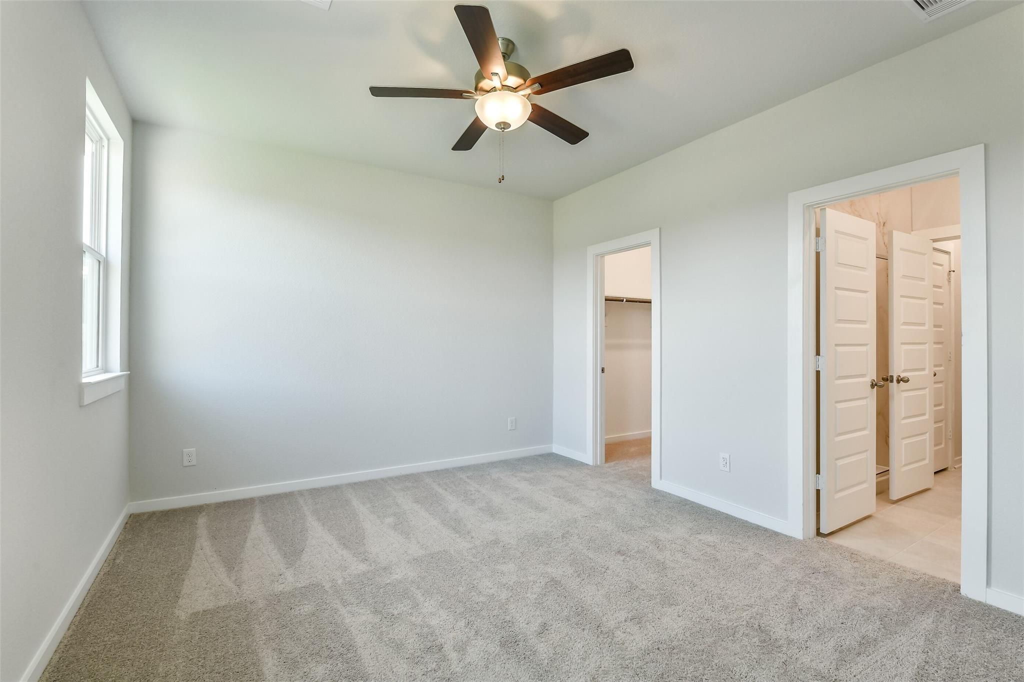 Bright secondary bedroom with ceiling fan, plush carpet, walk-in closet, and bathroom access in Davidson Homes The Colorado F, Cleveland, TX