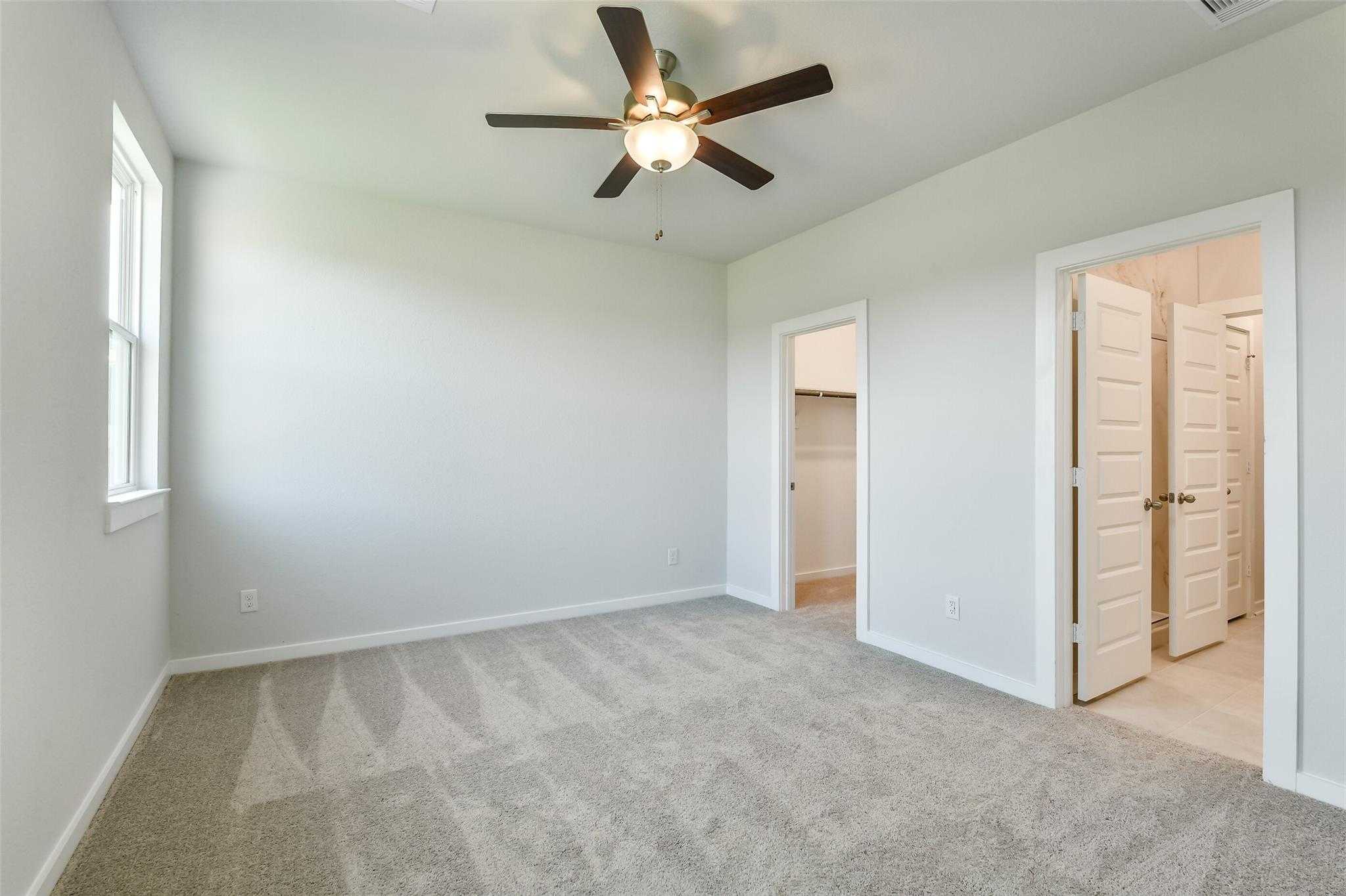Carpeted bedroom with ceiling fan, double doors to bathroom, and closet in Davidson Homes The Colorado F, Cleveland, Texas