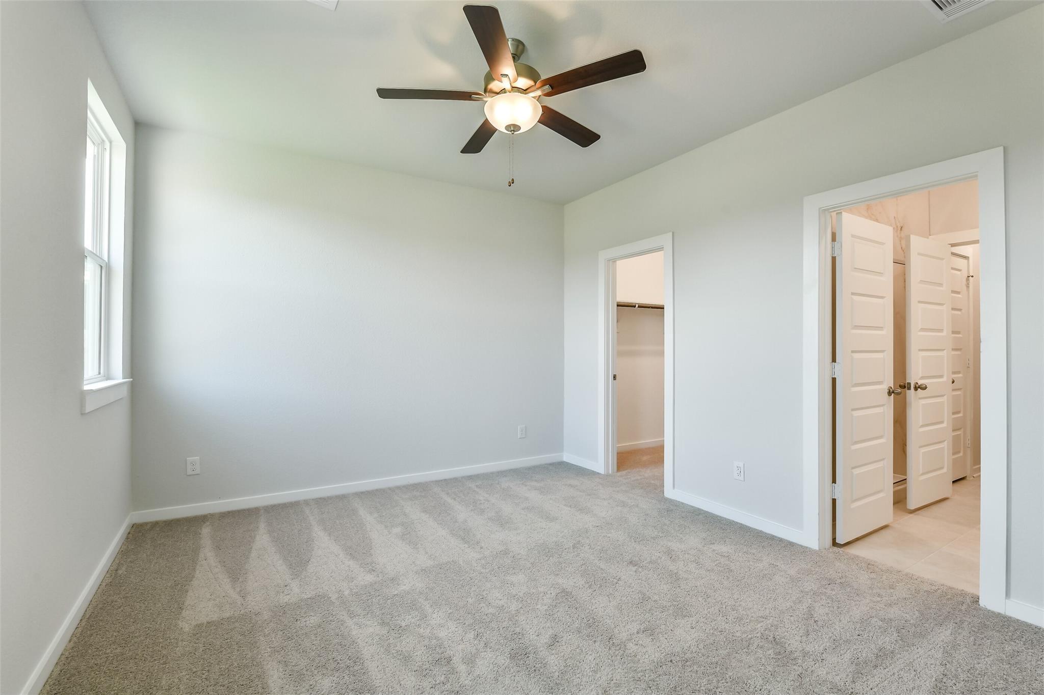 Carpeted secondary bedroom with ceiling fan, large window, closet, and bathroom access in Davidson Homes The Colorado F, Cleveland, Texas