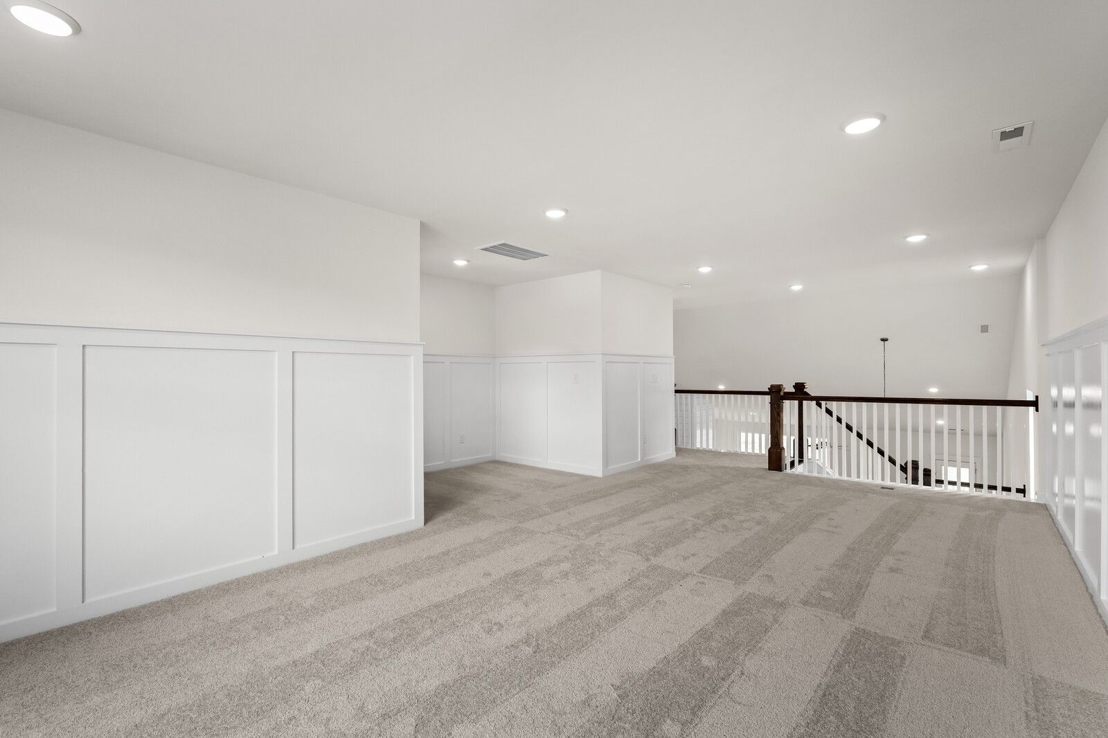 Spacious upstairs loft with white wainscoting, gray carpet, recessed lights, and wooden staircase in Davidson Homes The Ridgeport, Gallatin TN