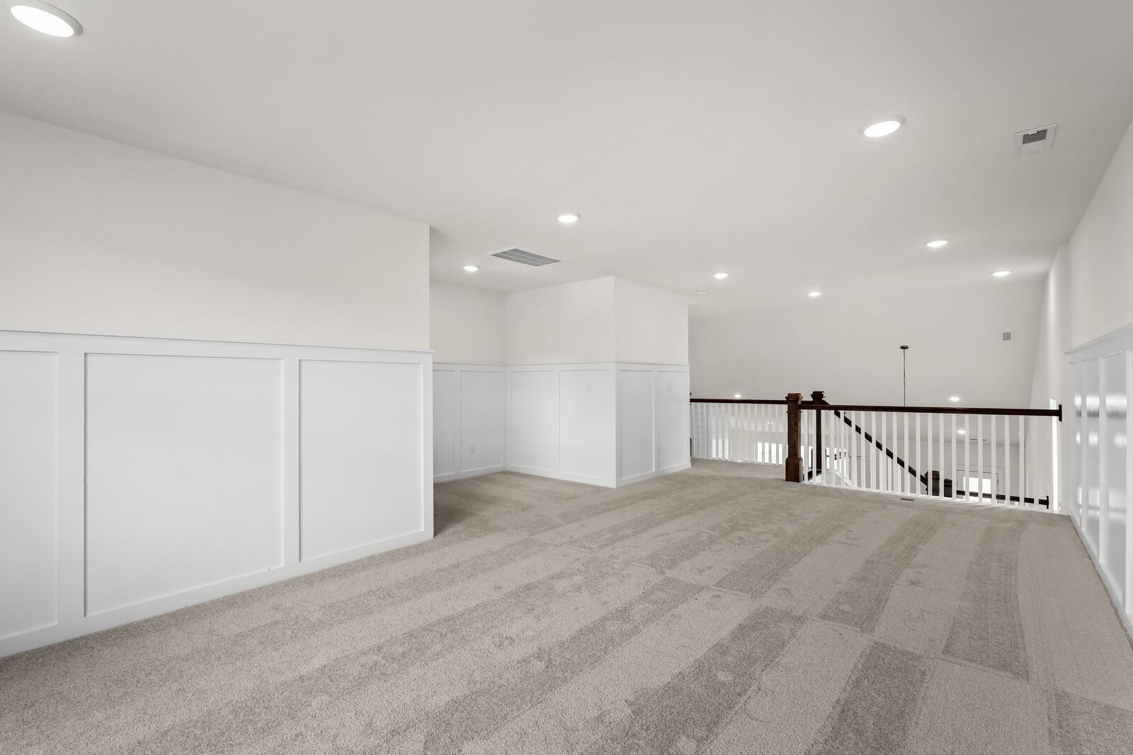 Spacious upstairs loft with white wainscoting, gray carpet, recessed lights, and wooden staircase in Davidson Homes The Ridgeport, Gallatin TN