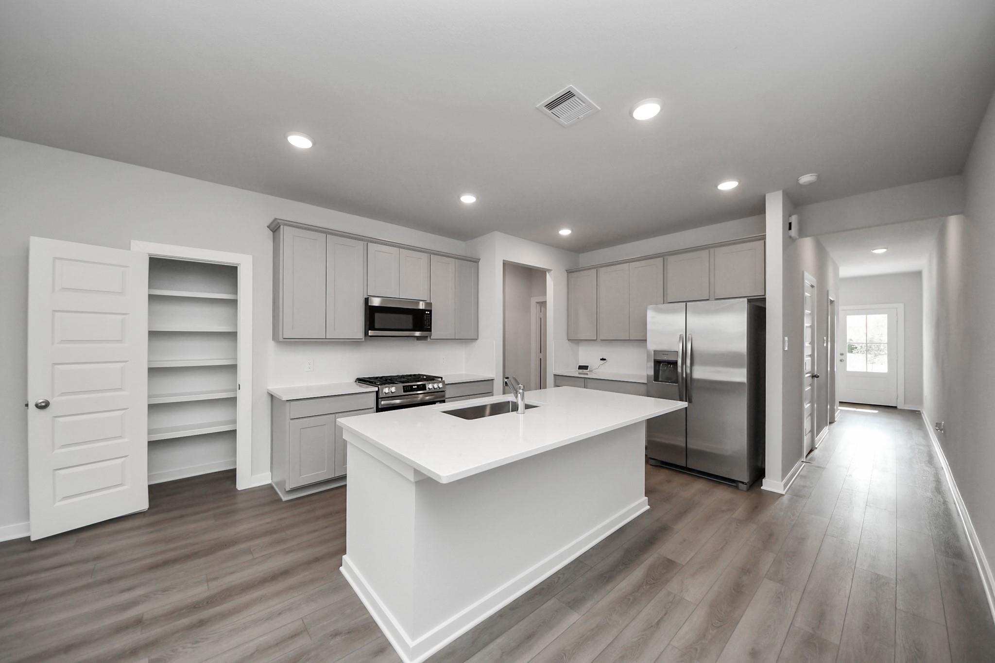 Modern kitchen with large island, gray shaker cabinets, stainless appliances, and walk-in pantry in Davidson Homes The Frio F, Houston