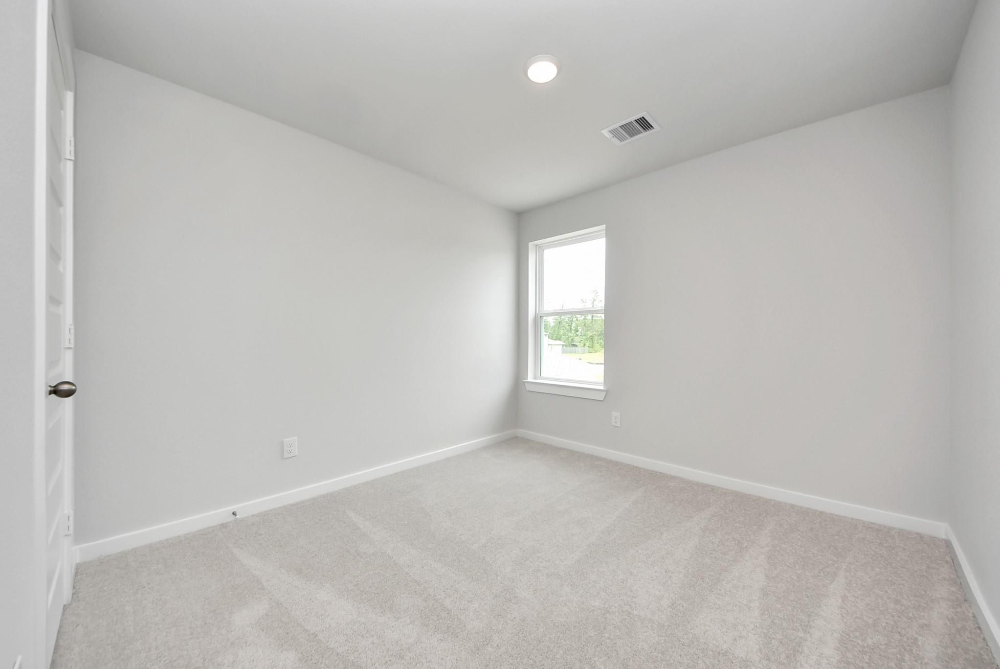 Bright, carpeted bedroom with neutral walls in The Blanco E floor plan at The Villages at WestPointe in Dayton, Texas.