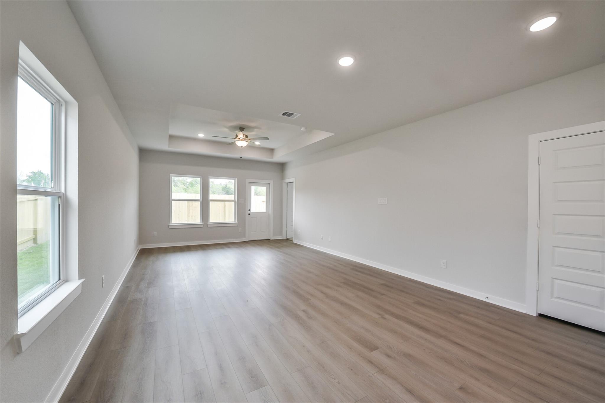 Spacious open hallway with laminate wood floors, large windows, and ceiling fan in Davidson Homes The Frio F, Conroe, Texas