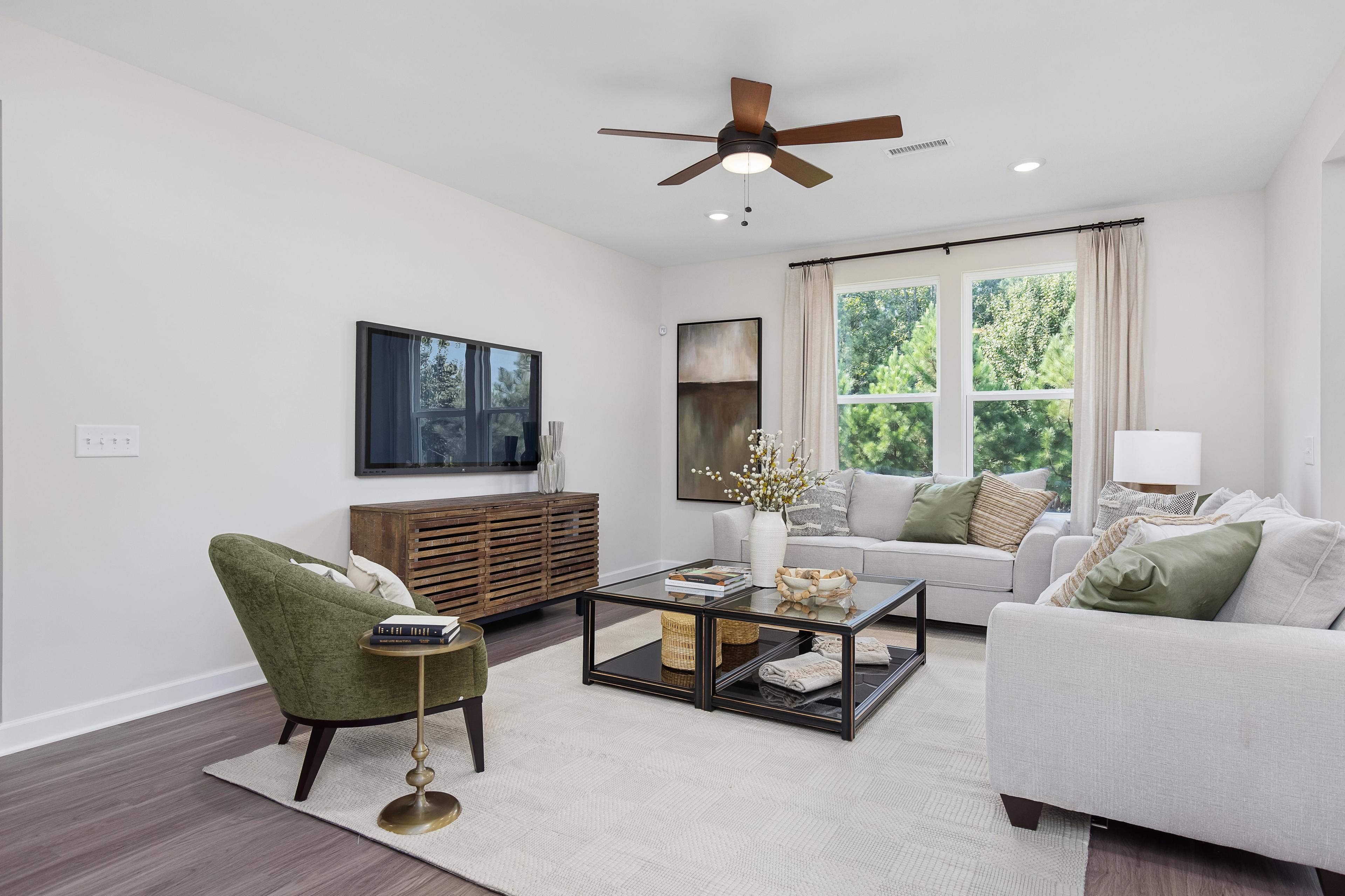 Cozy living room at Woodland Crossing in Zebulon NC with neutral sofa, green accent chair, hardwood floors, and large tree-view windows