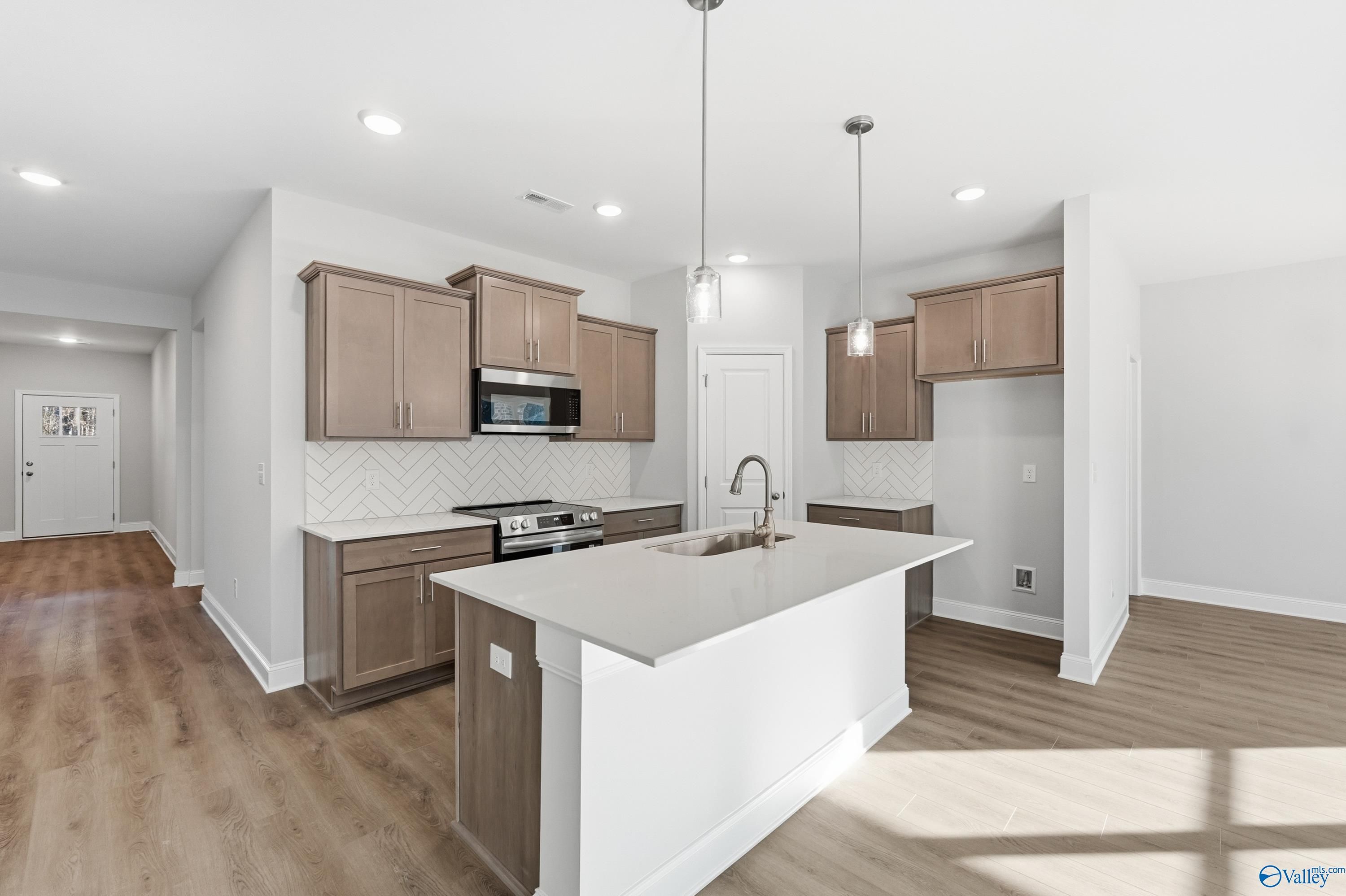 Modern kitchen with light wood cabinets, white quartz island, stainless appliances, and subway tile backsplash in The Daphne C, Arab, Alabama