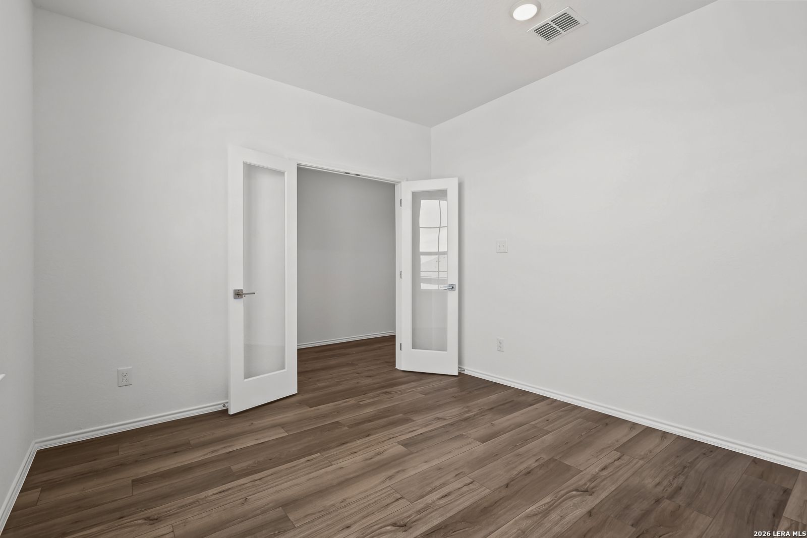 Bright empty room with white walls, hardwood floors, and open French doors in Davidson Homes The Sequoia B, Comanche Ridge, San Antonio