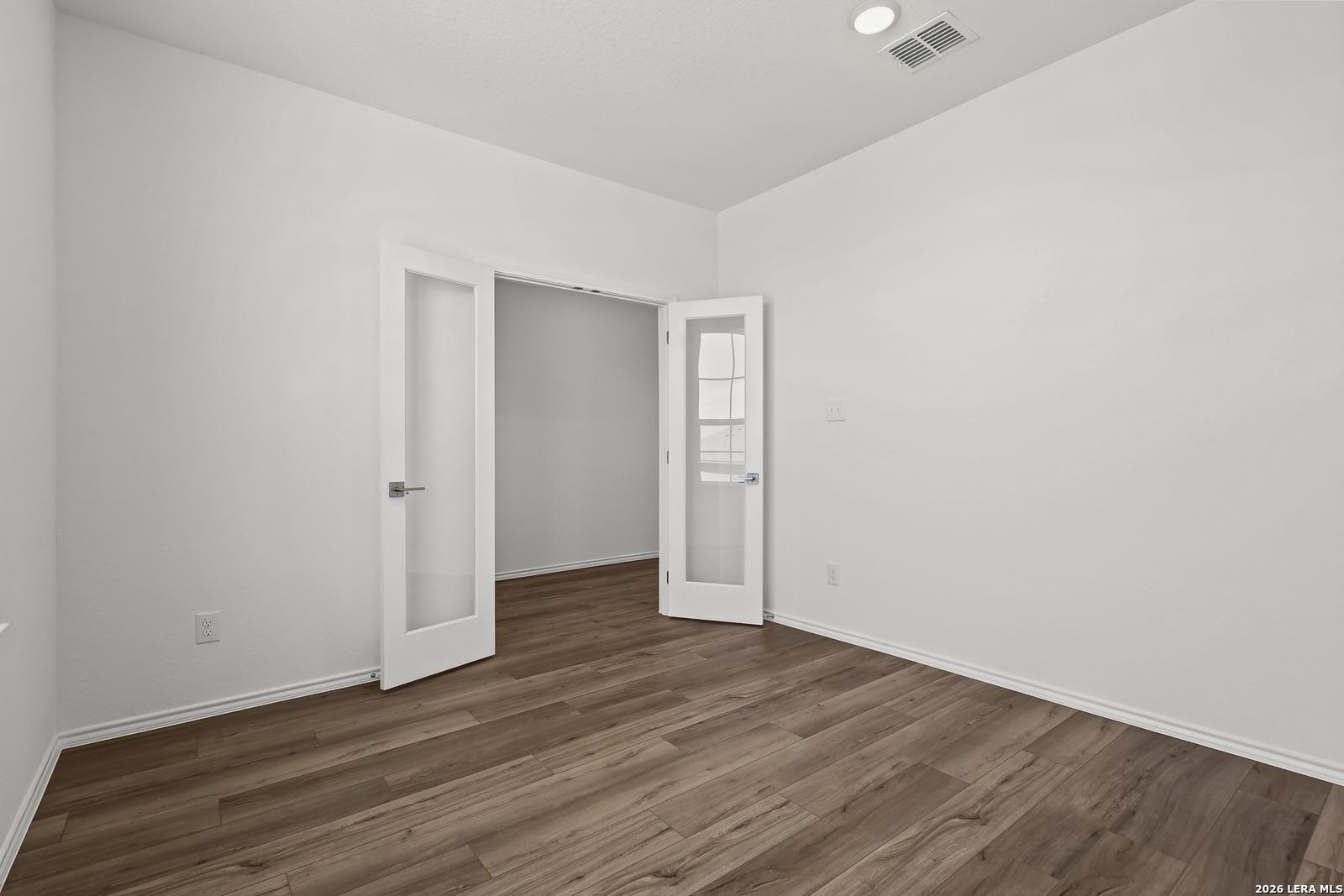 Bright empty room with white walls, hardwood floors, and open French doors in Davidson Homes The Sequoia B, Comanche Ridge, San Antonio