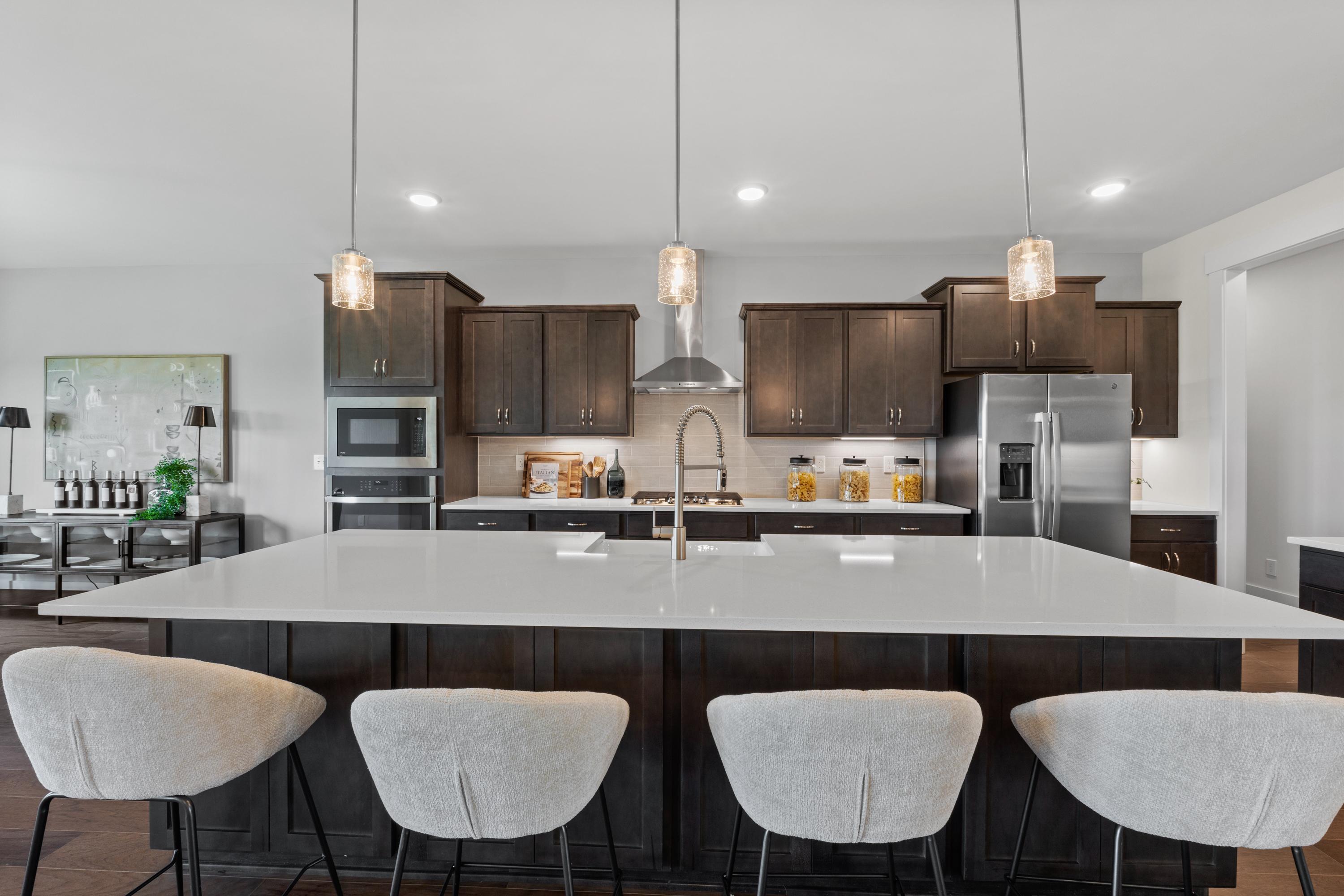 Modern kitchen at Creekside in Harvest Alabama with white quartz island, dark wood cabinets, stainless appliances, and pendant lights