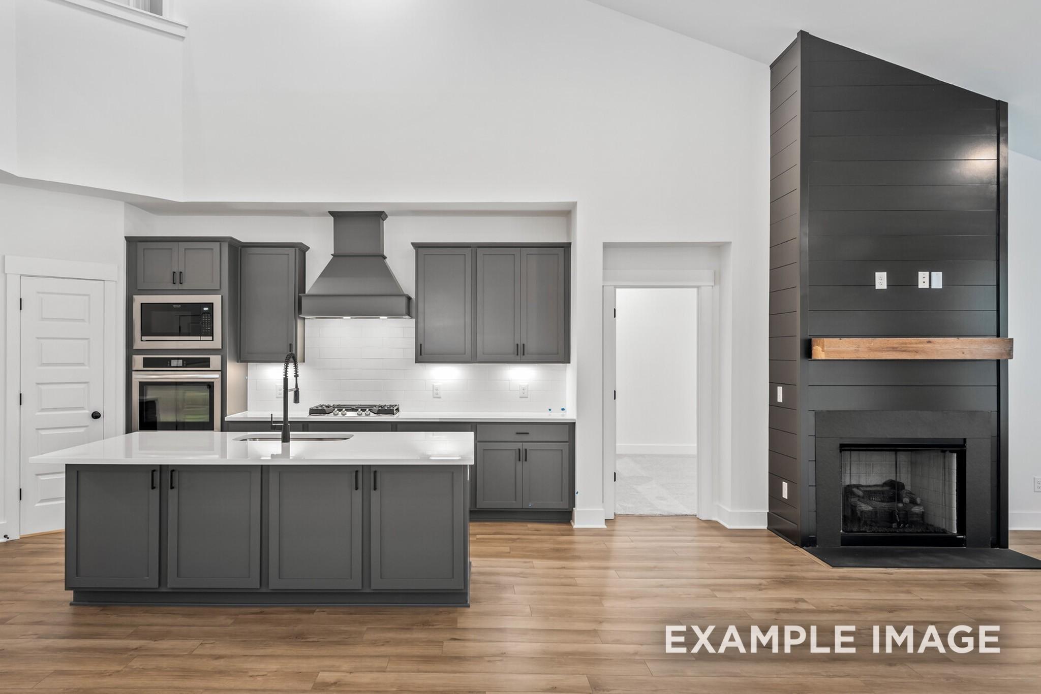 Modern open-concept kitchen with gray cabinets, large island, stainless appliances, and adjacent living room fireplace in The Ridgeport C, Gallatin, TN