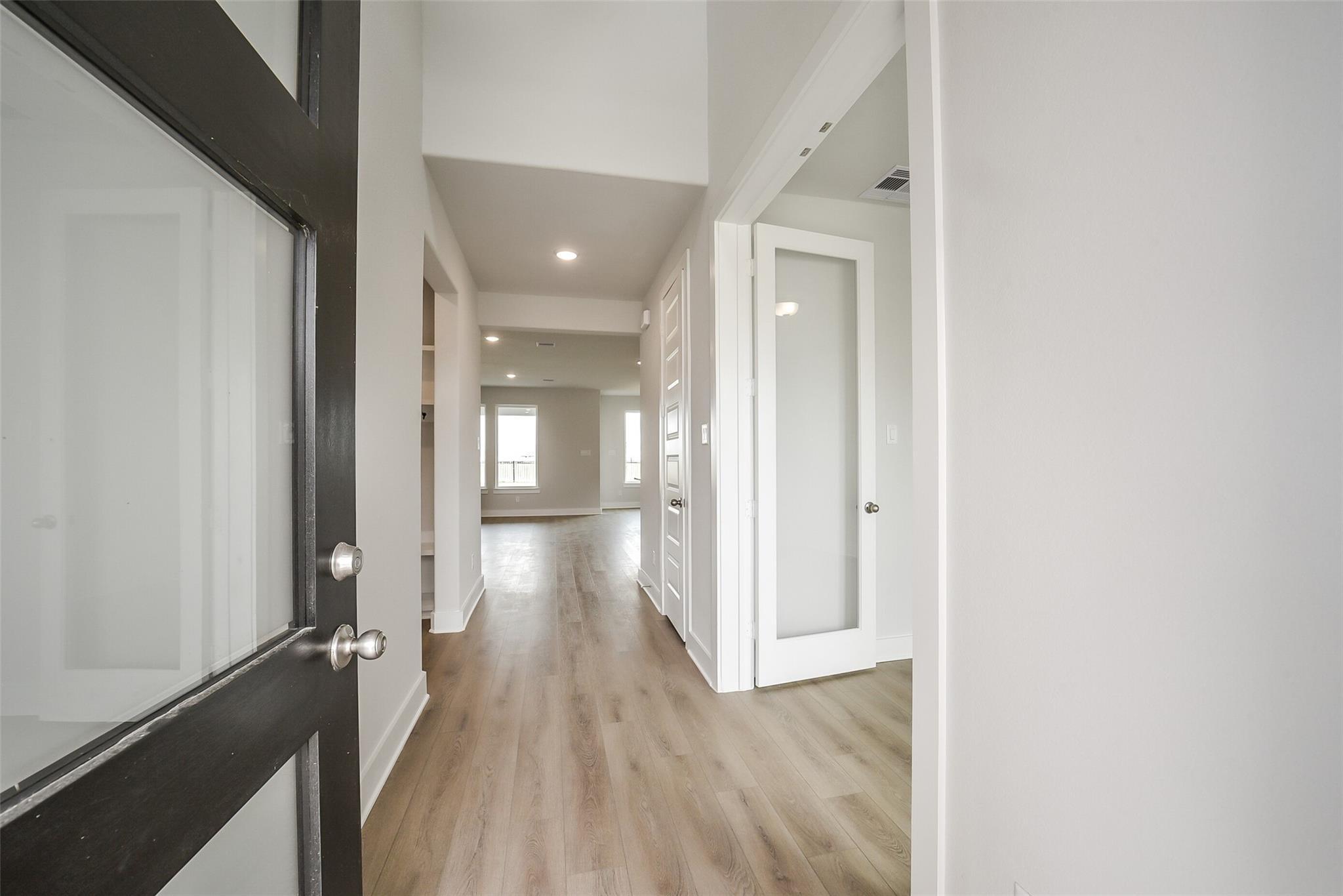 Welcoming entry foyer with light hardwood floors, high ceilings, and glass-paneled doors in Davidson Homes The Philip B, Rosharon, Texas