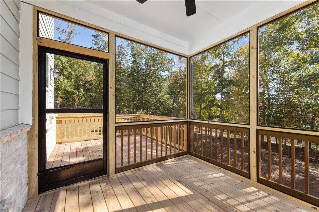 Screened porch with wooden deck, ceiling fan, and black door overlooking wooded backyard in Davidson Homes The Danbury C, Buford, Georgia