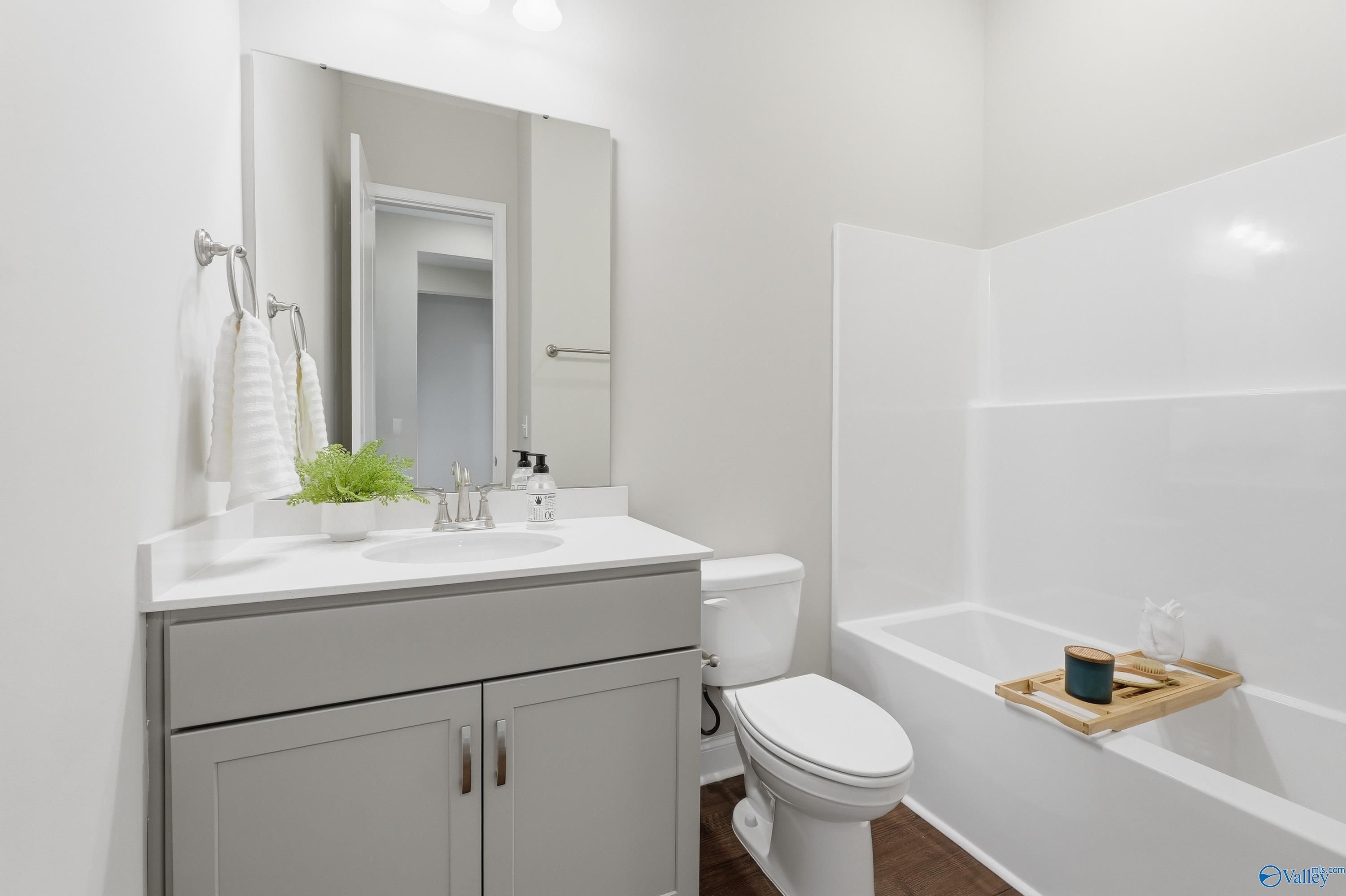 Modern guest bathroom with gray vanity, white soaking tub, wooden caddy, and plants in Davidson Homes The Arcadia B, Huntsville