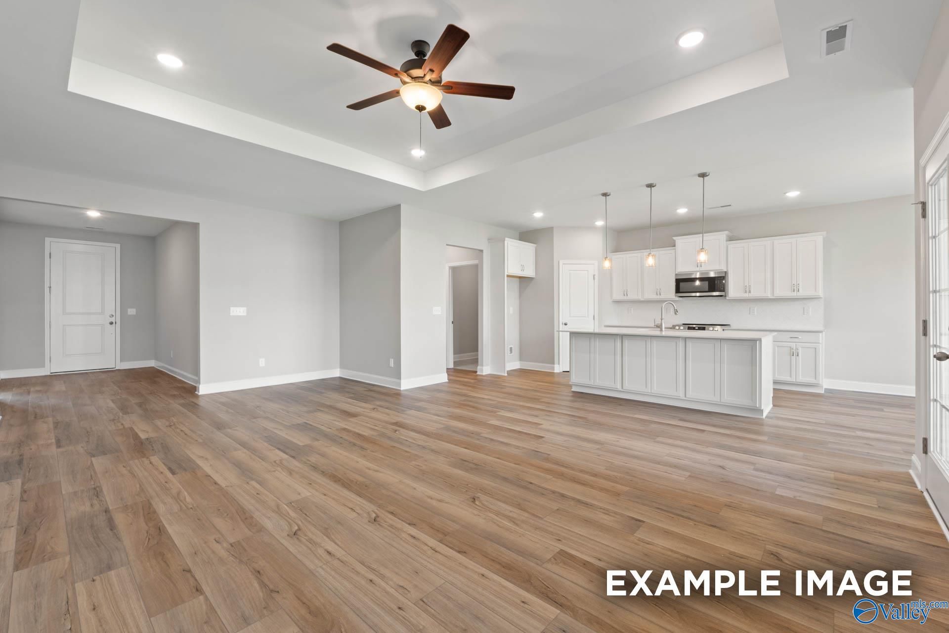 Open-concept kitchen and living space with white shaker cabinets, large island, luxury vinyl plank floors, and ceiling fan in Davidson Homes Montgomery B, Hartselle, AL