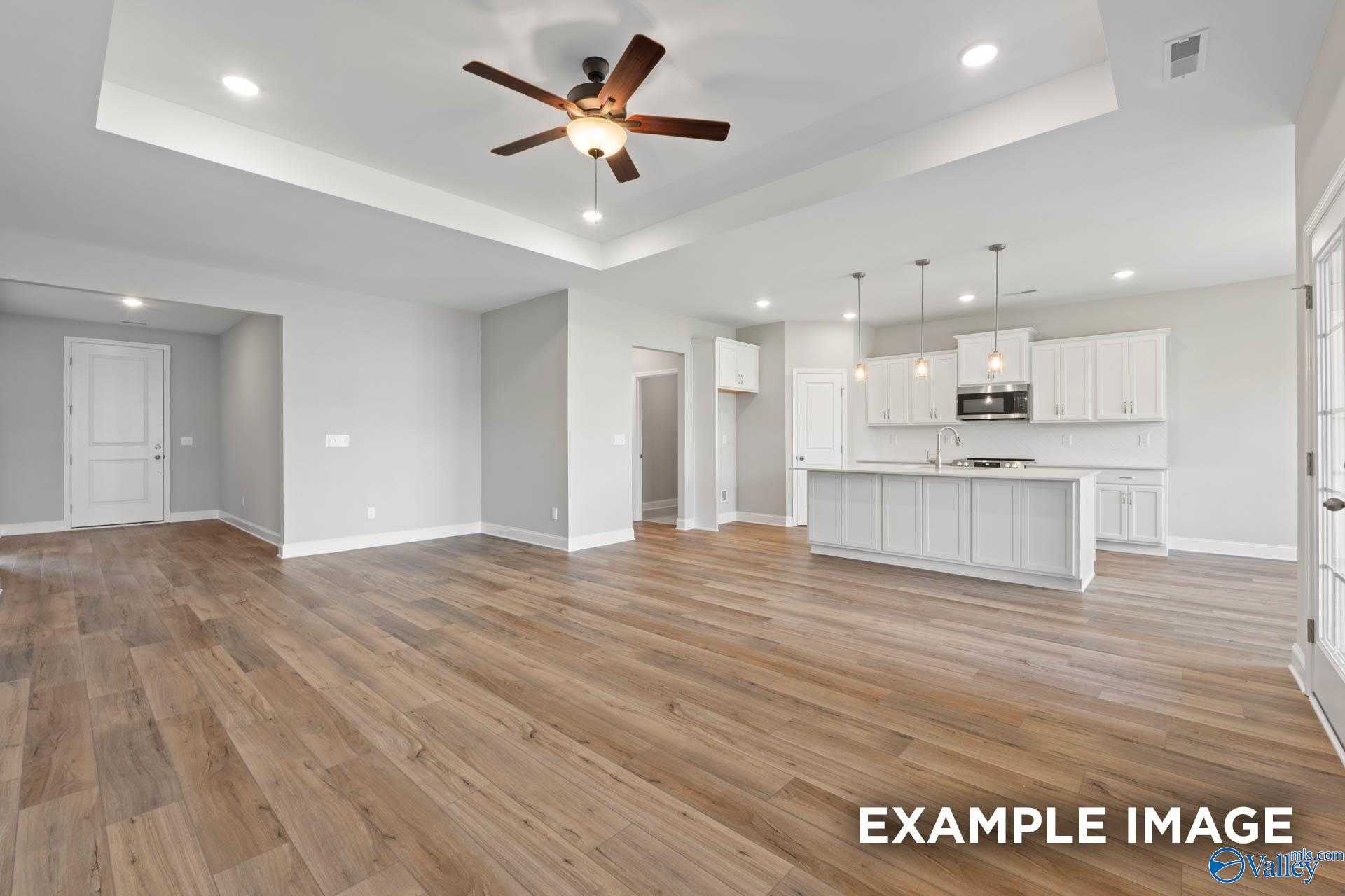 Open-concept kitchen and living space with white shaker cabinets, large island, luxury vinyl plank floors, and ceiling fan in Davidson Homes Montgomery B, Hartselle, AL
