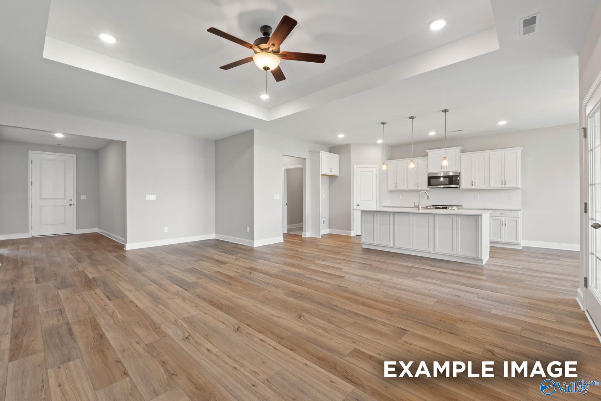 Open-concept living-kitchen with hardwood floors, white island cabinets, pendant lights, and ceiling fan in Davidson Homes Montgomery B, Hartselle AL