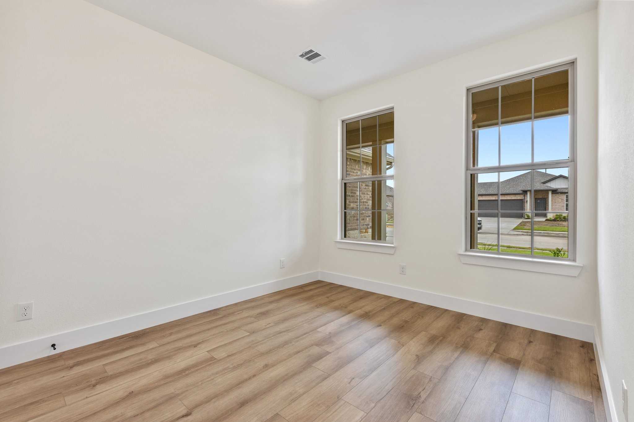 Bright empty bedroom with large windows, light wood floors, and white walls in Davidson Homes The Rockford C, Waverly Estates, Josephine, Texas