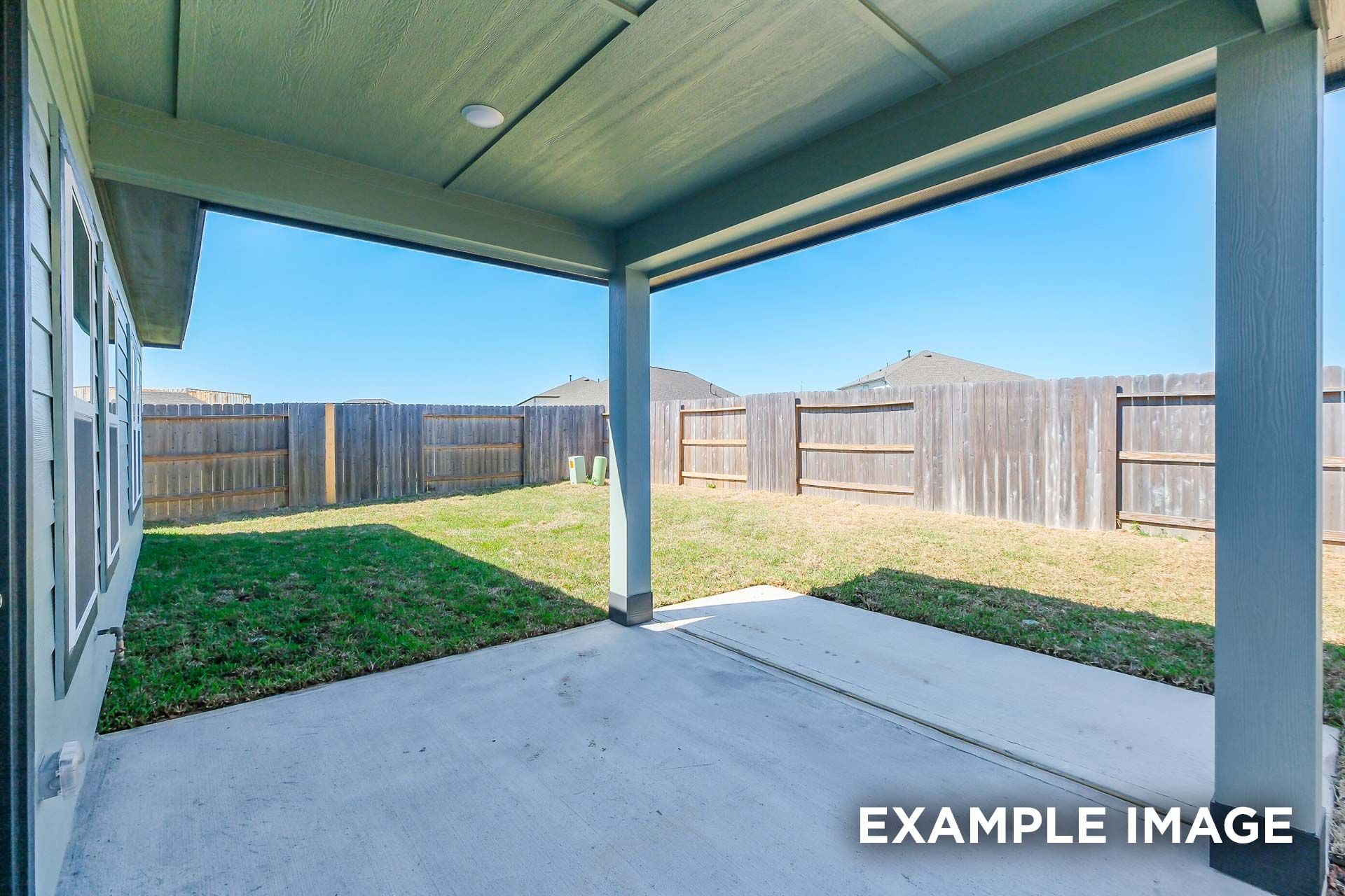Spacious covered patio of The Luna K home with concrete floor, green roof, grassy backyard, and wood fence in Katy Texas