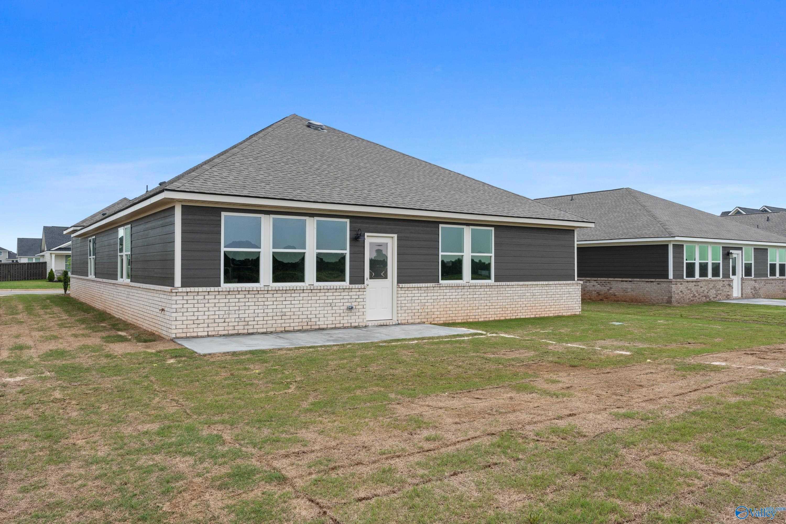 Modern gray-sided 1-story home with brick accents, large windows, side door, and concrete patio in Anderson Farm, Athens, Alabama - Davidson Homes The Orion