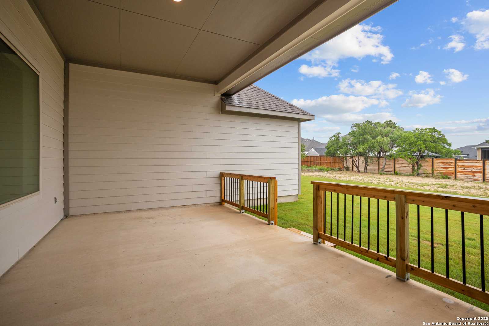Covered back patio with wooden deck railing overlooking grassy yard and trees in The Summerlin B, Potranco Oaks, Castroville, Texas