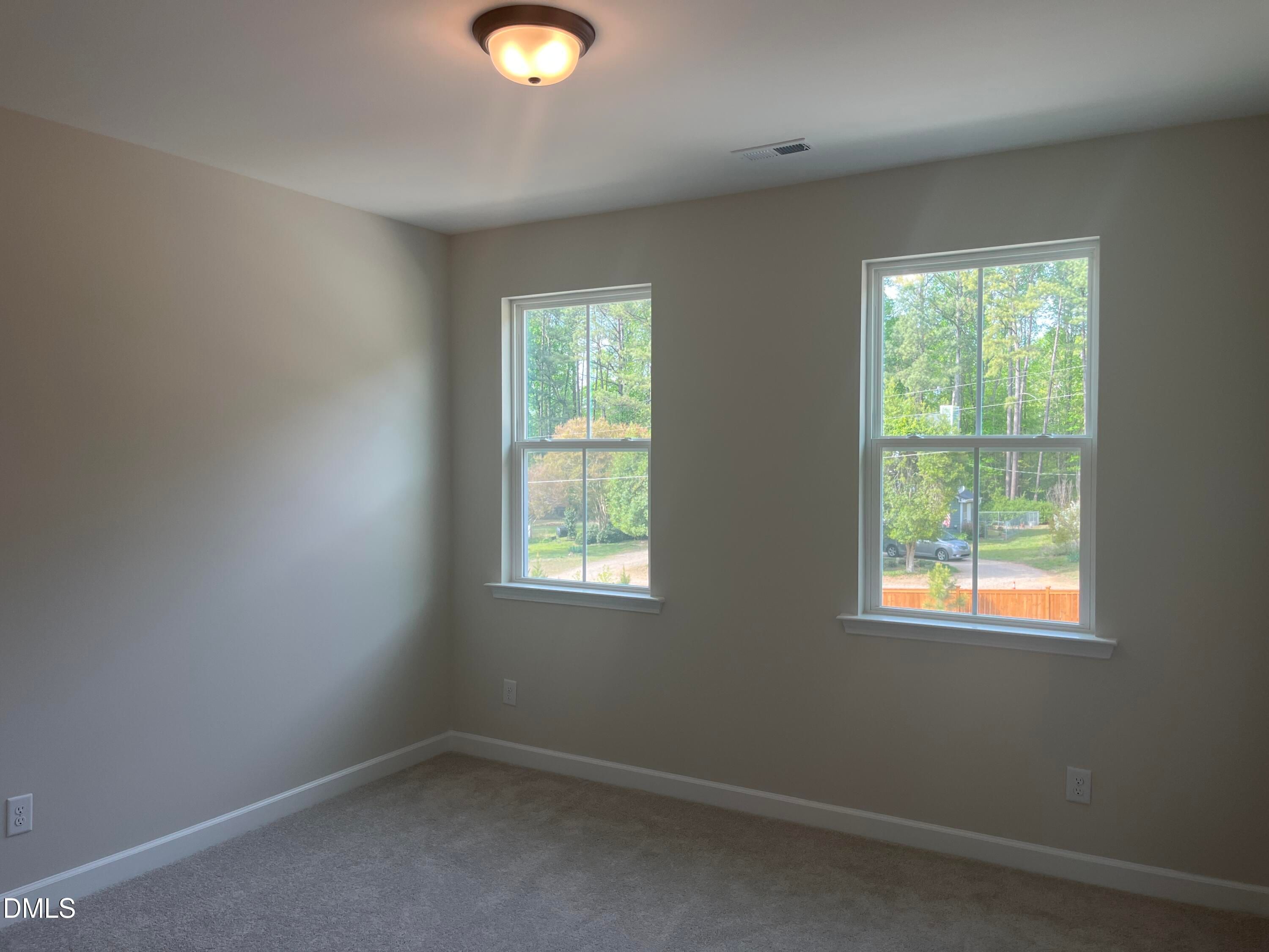 Bright secondary bedroom with beige walls, carpet floor, and large windows showing wooded backyard in Davidson Homes Ashport L, Wake Forest NC